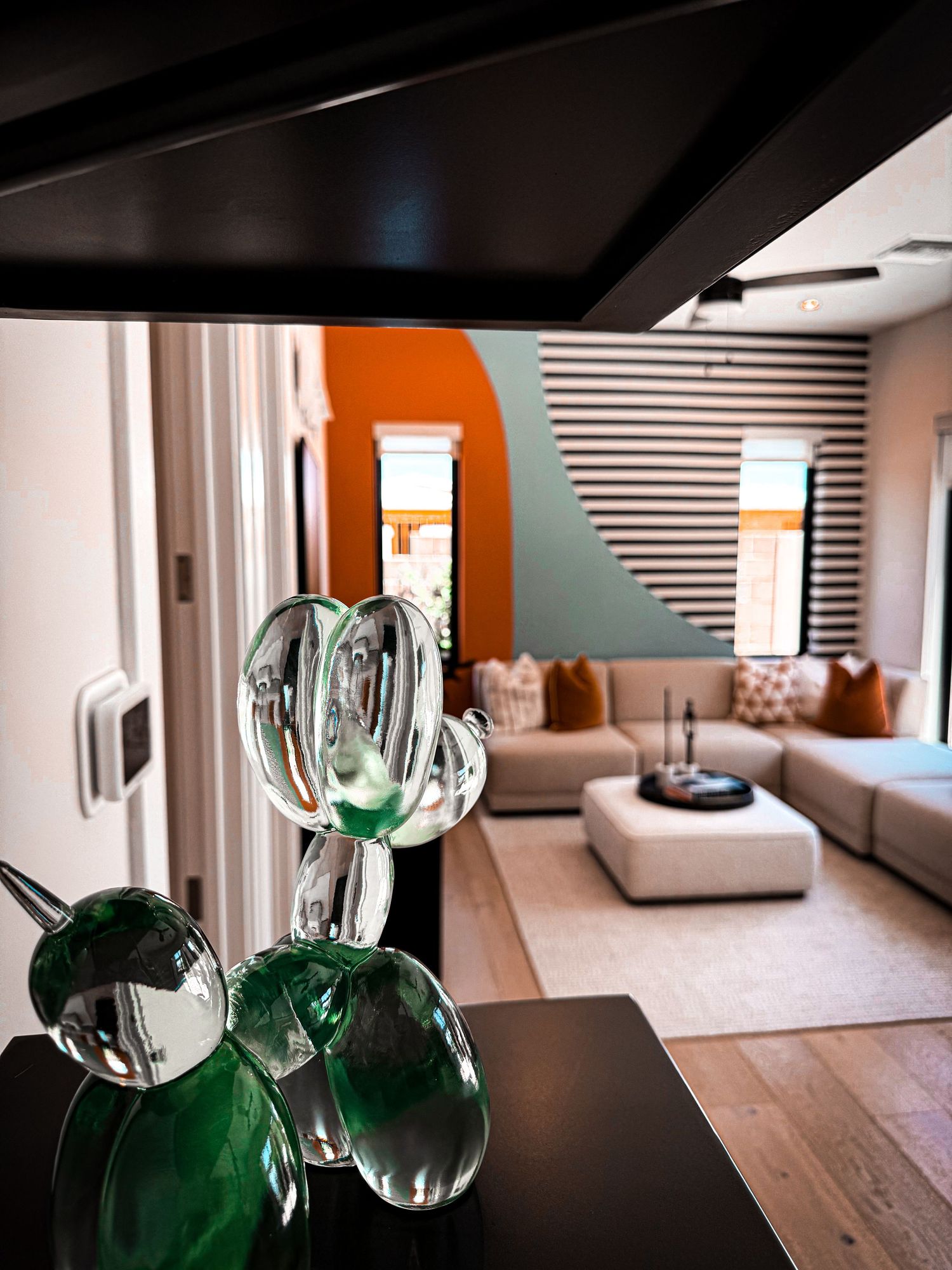 Modern living room with glass cactus sculpture, striped accent wall, sectional sofa, and bold orange and teal color accents.