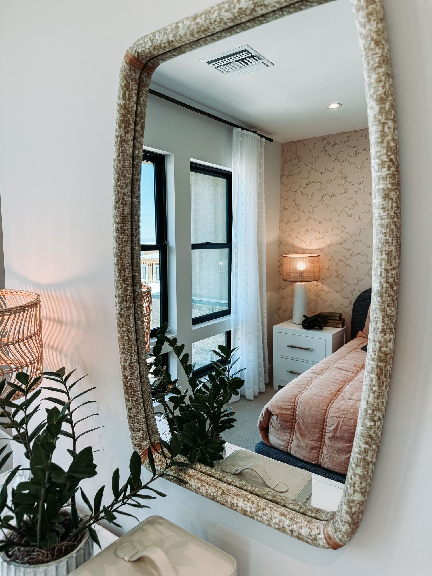 Decorative mosaic-framed mirror reflecting a cozy bedroom with pink bedding, white dresser, and warm lamp lighting.