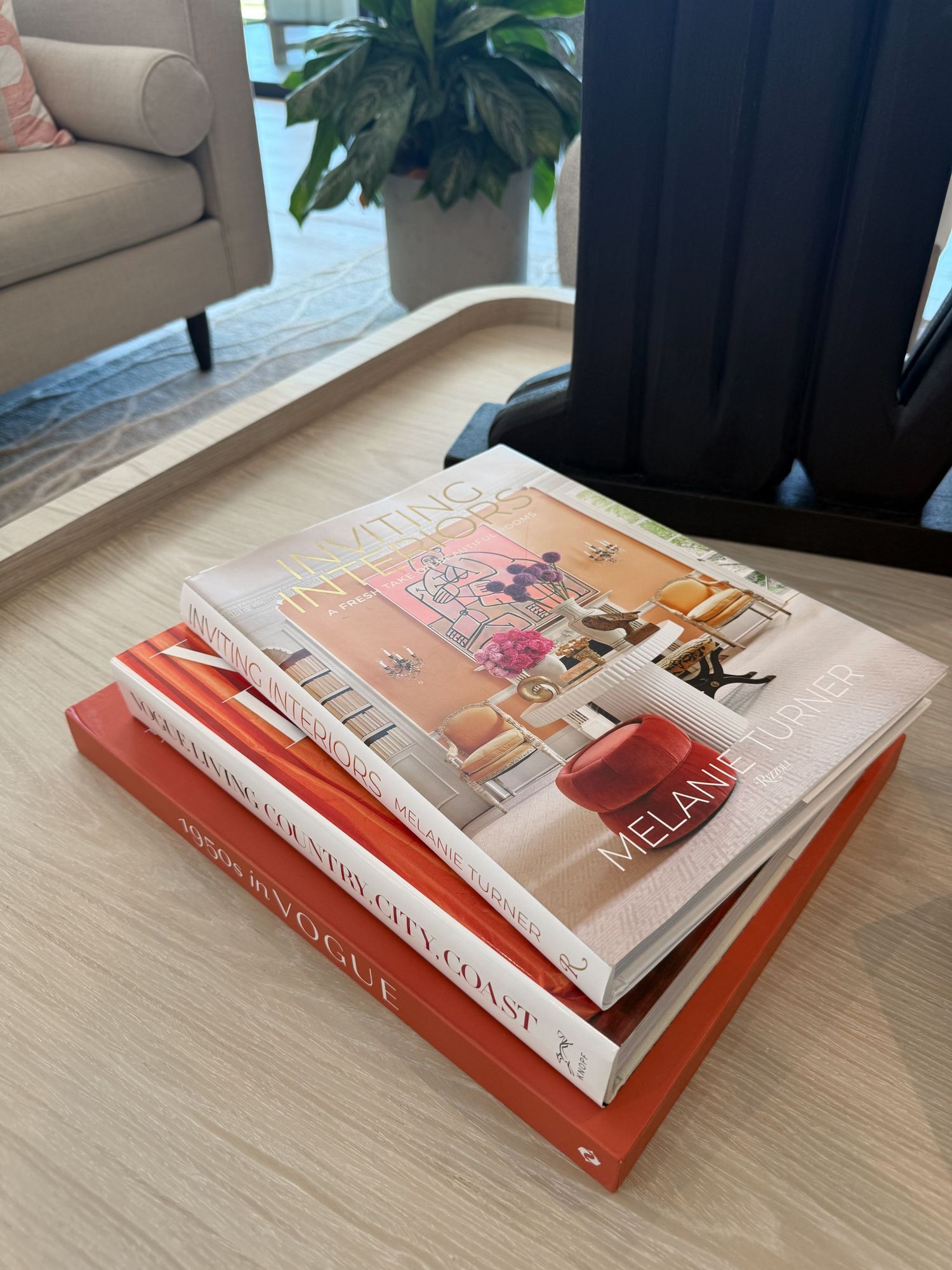 Stack of three coffee table books on a wooden table, including titles by Melanie Turner and Vogue, in a modern living room.