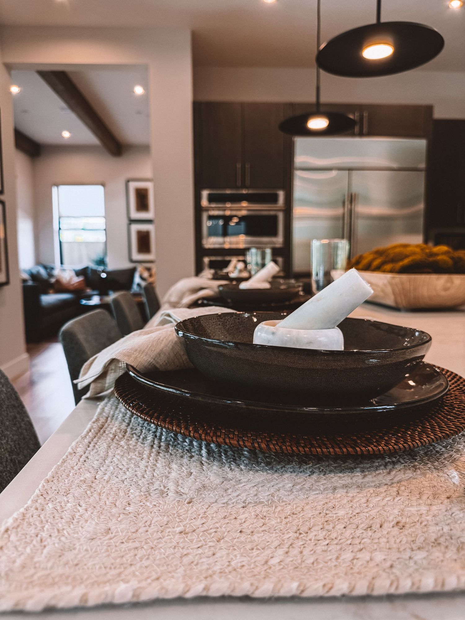 Modern open-concept dining area with dark ceramic plates, pendant lights, and stainless steel kitchen appliances in background.