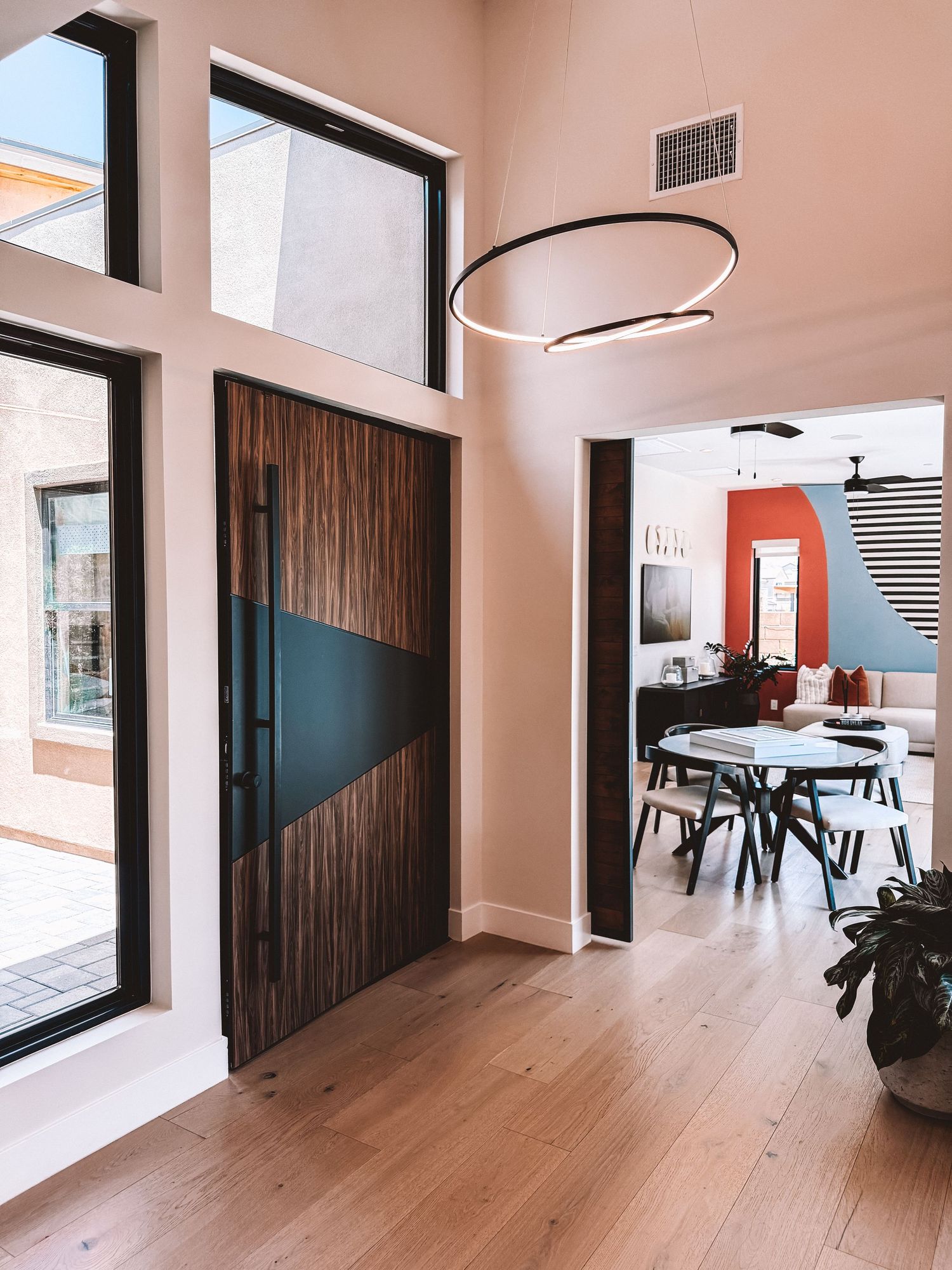 Modern home entryway with wood and black front door, circular pendant light, and open dining area with bold accent wall.