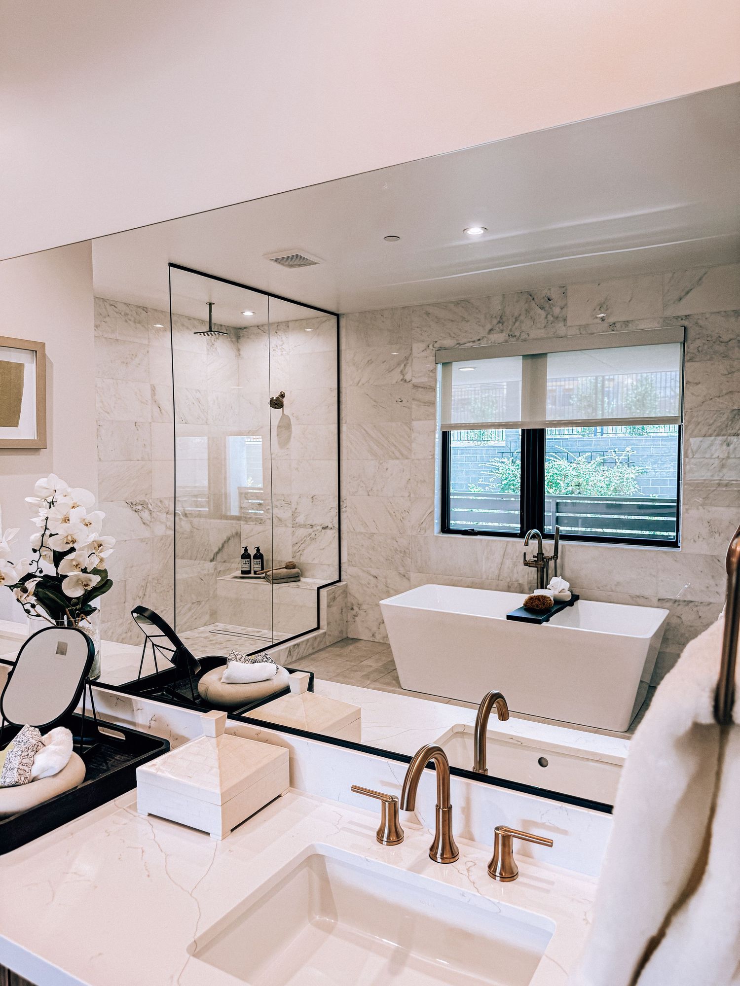 Luxury marble bathroom with freestanding soaking tub, glass shower, and gold faucets in an elegant white space.