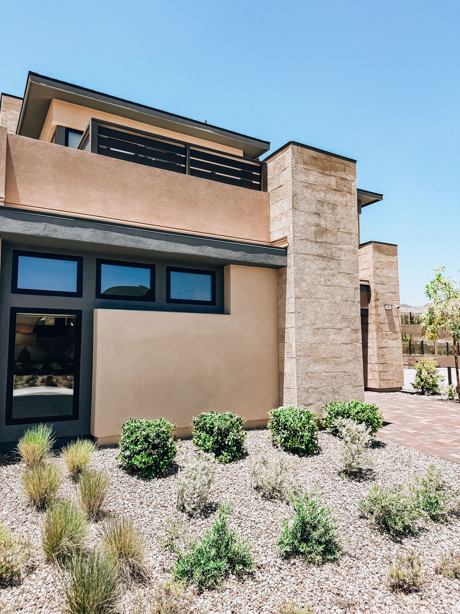 Modern desert home with stucco exterior, stone pillars, and xeriscape landscaping featuring ornamental grasses and shrubs.