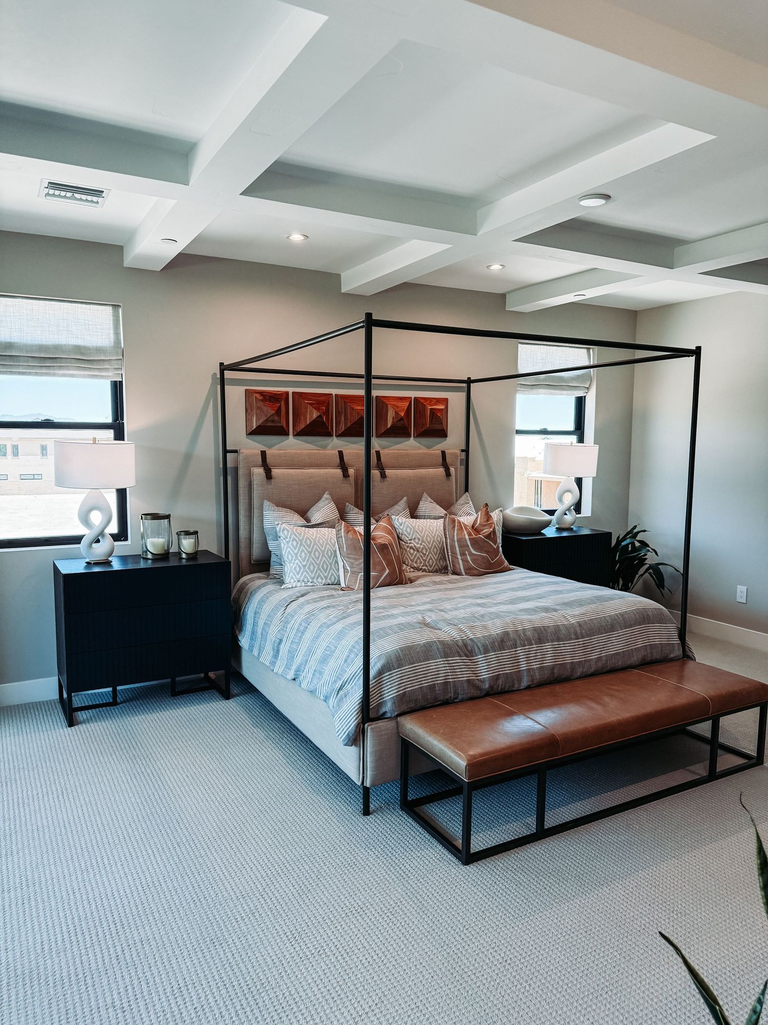 Modern four-poster canopy bed in a luxurious master bedroom with coffered ceiling, neutral tones, and leather bench.