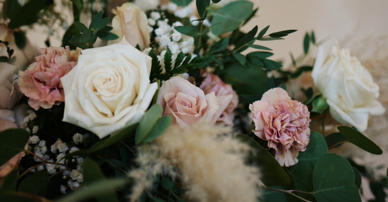 Close-up of a bridal bouquet with white roses, dusty pink carnations, greenery, and baby's breath.