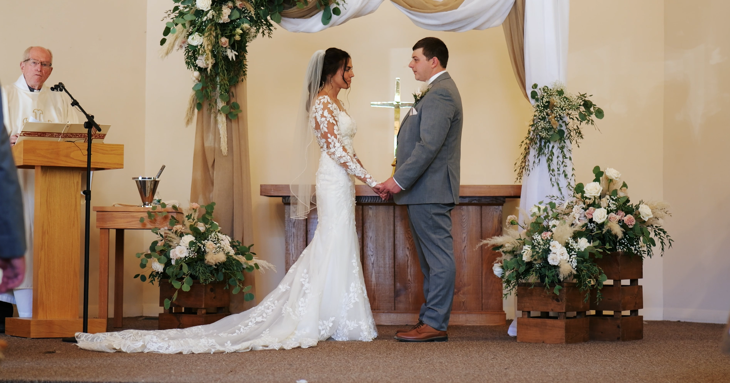 Bride and groom holding hands at the altar during their wedding ceremony in a white chapel.