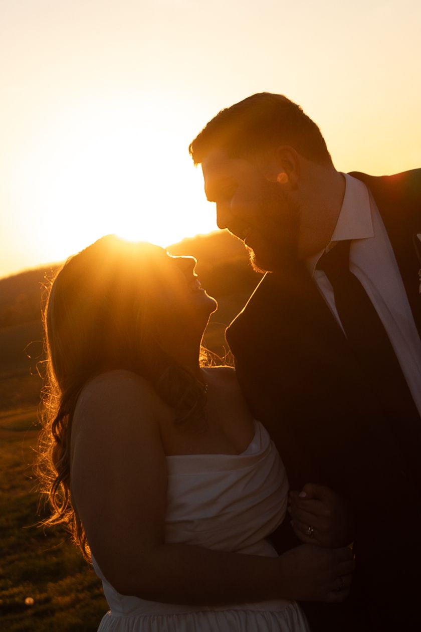 Romantic silhouette of a bride and groom nearly kissing against a glowing sunset.