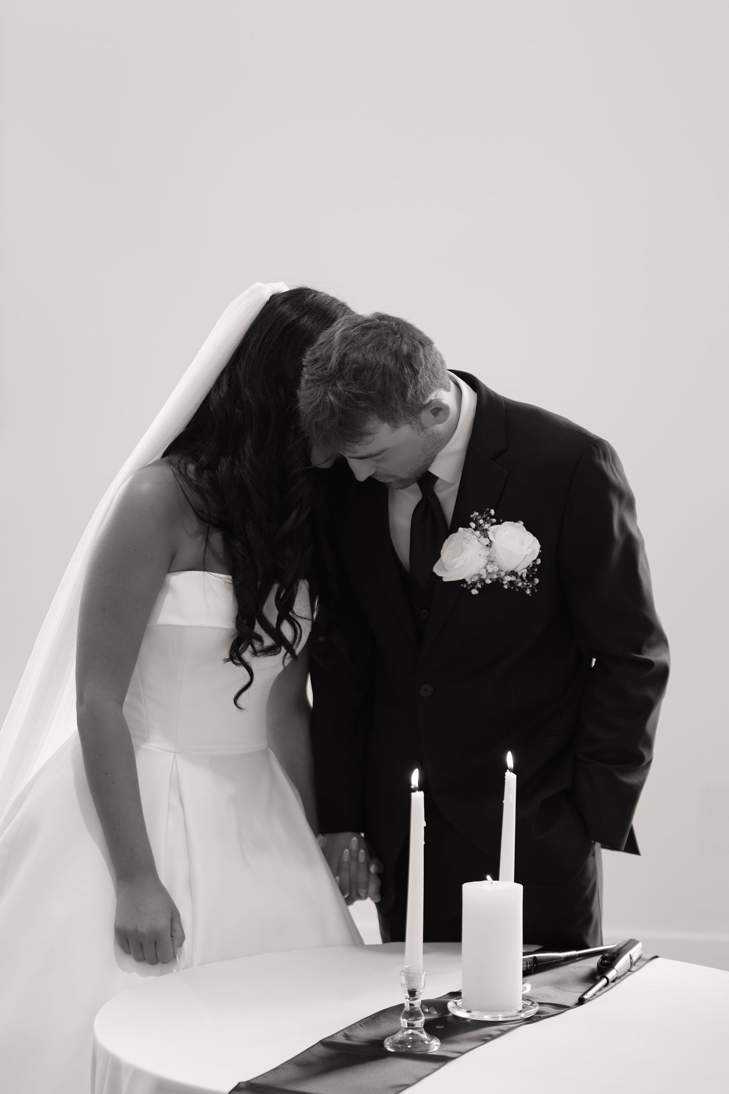 Black and white photo of bride and groom signing wedding register with two white candles on table.