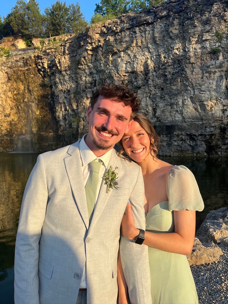 Smiling couple in formal attire posing in front of rocky cliffs at a wedding.