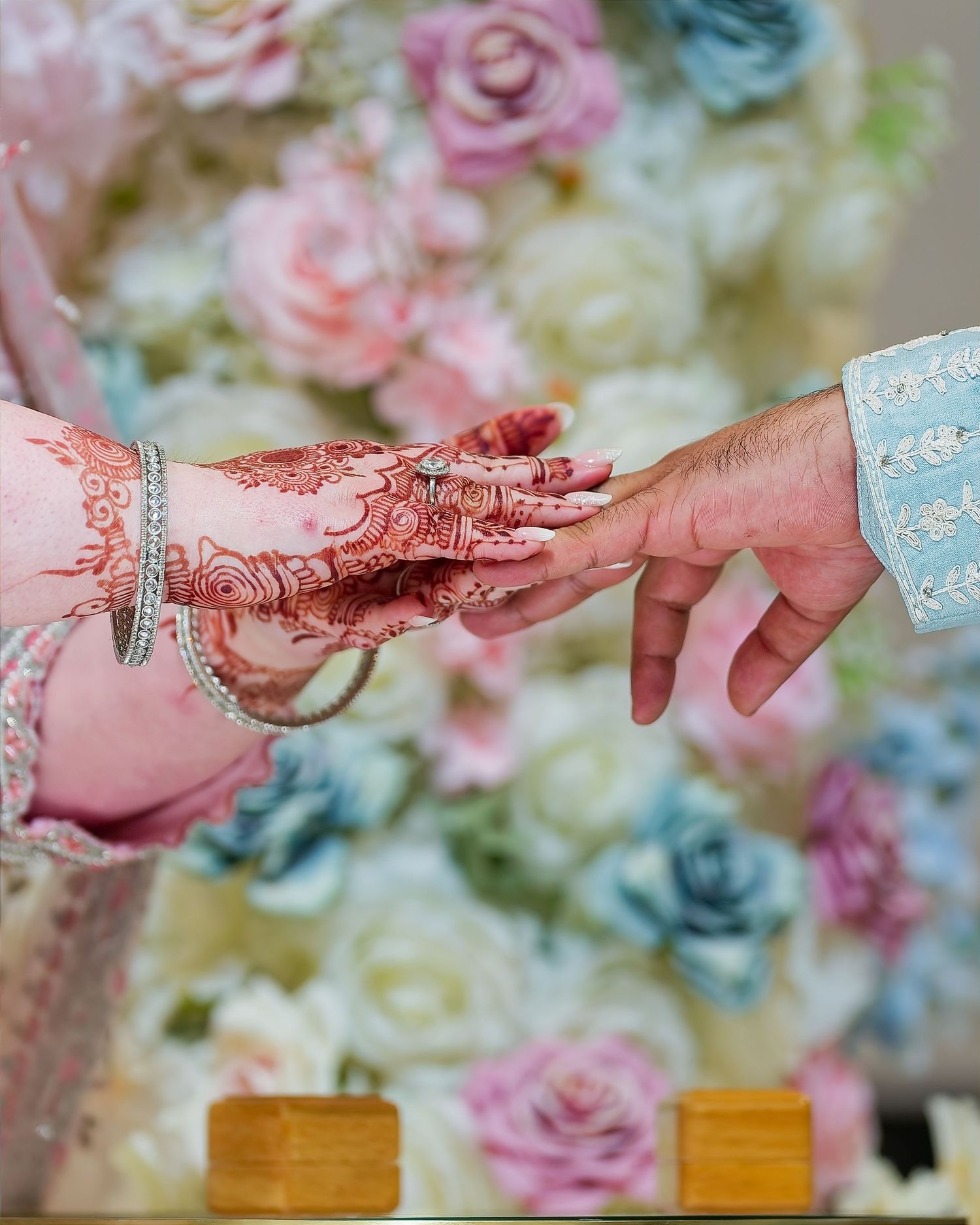 Bride with intricate henna hands exchanging rings against colorful floral backdrop.