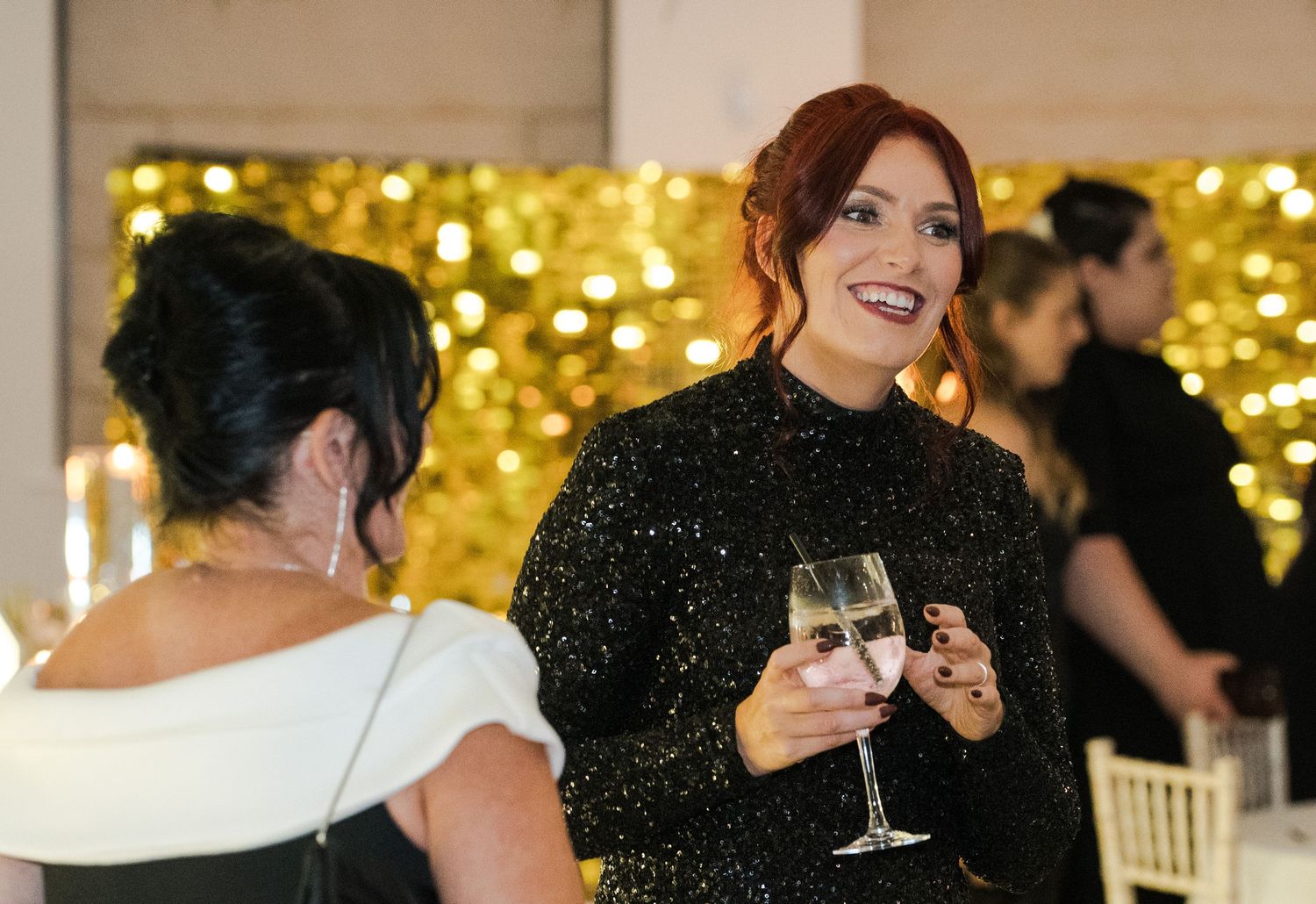 Elegant woman in a black sequin dress holding champagne glass at a glamorous wedding reception.