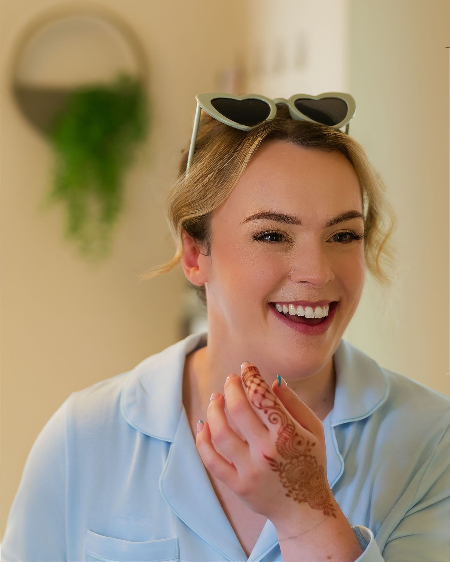 Smiling blonde woman with henna hand art and heart sunglasses enjoying wedding celebrations.