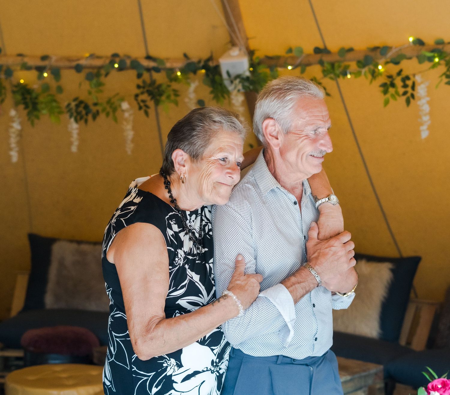 Elderly couple shares a dance together smiling under fairy lights at wedding reception tent.