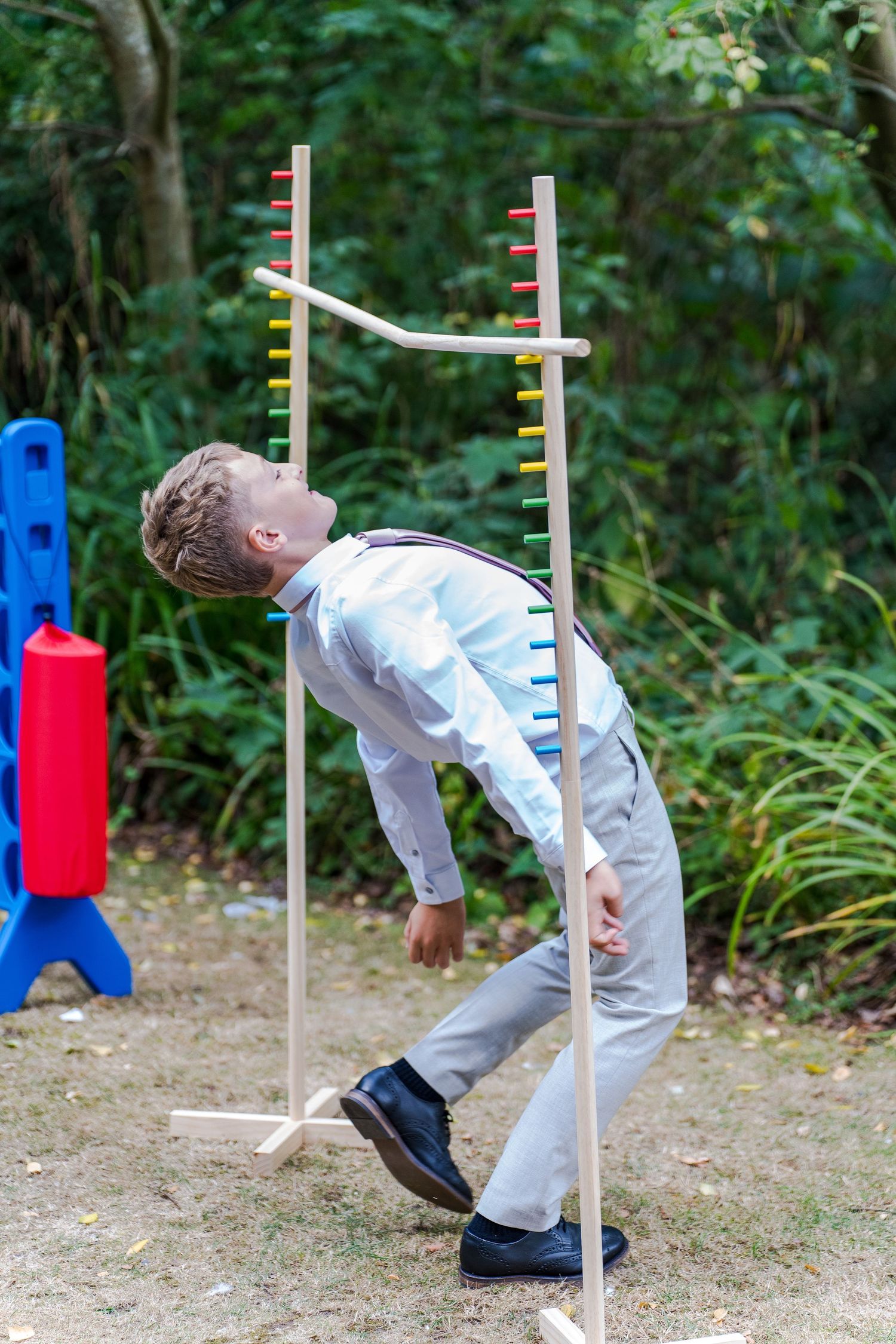 A young boy in formal attire bends backward under a limbo bar at an outdoor wedding reception game.