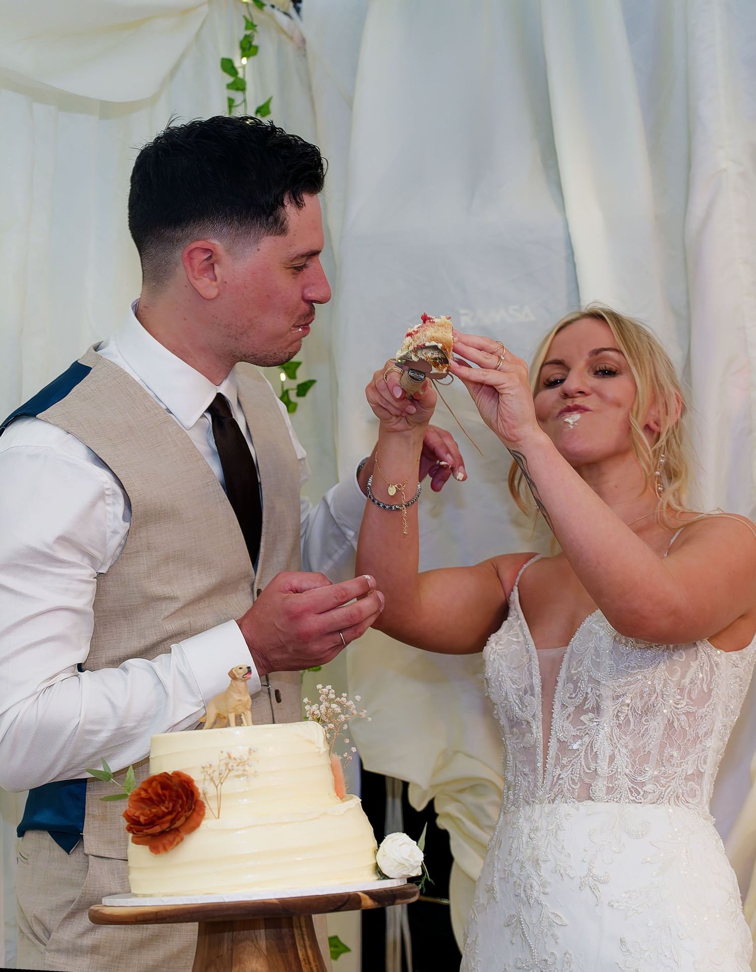 Bride and groom playfully feeding each other wedding cake at their outdoor wedding celebration.