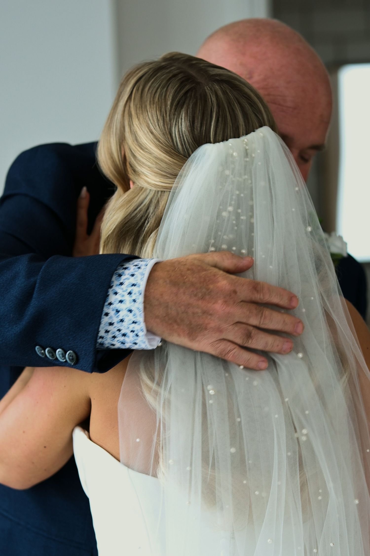 Father of the bride sharing a tender embrace with his daughter in her pearl-adorned wedding veil.