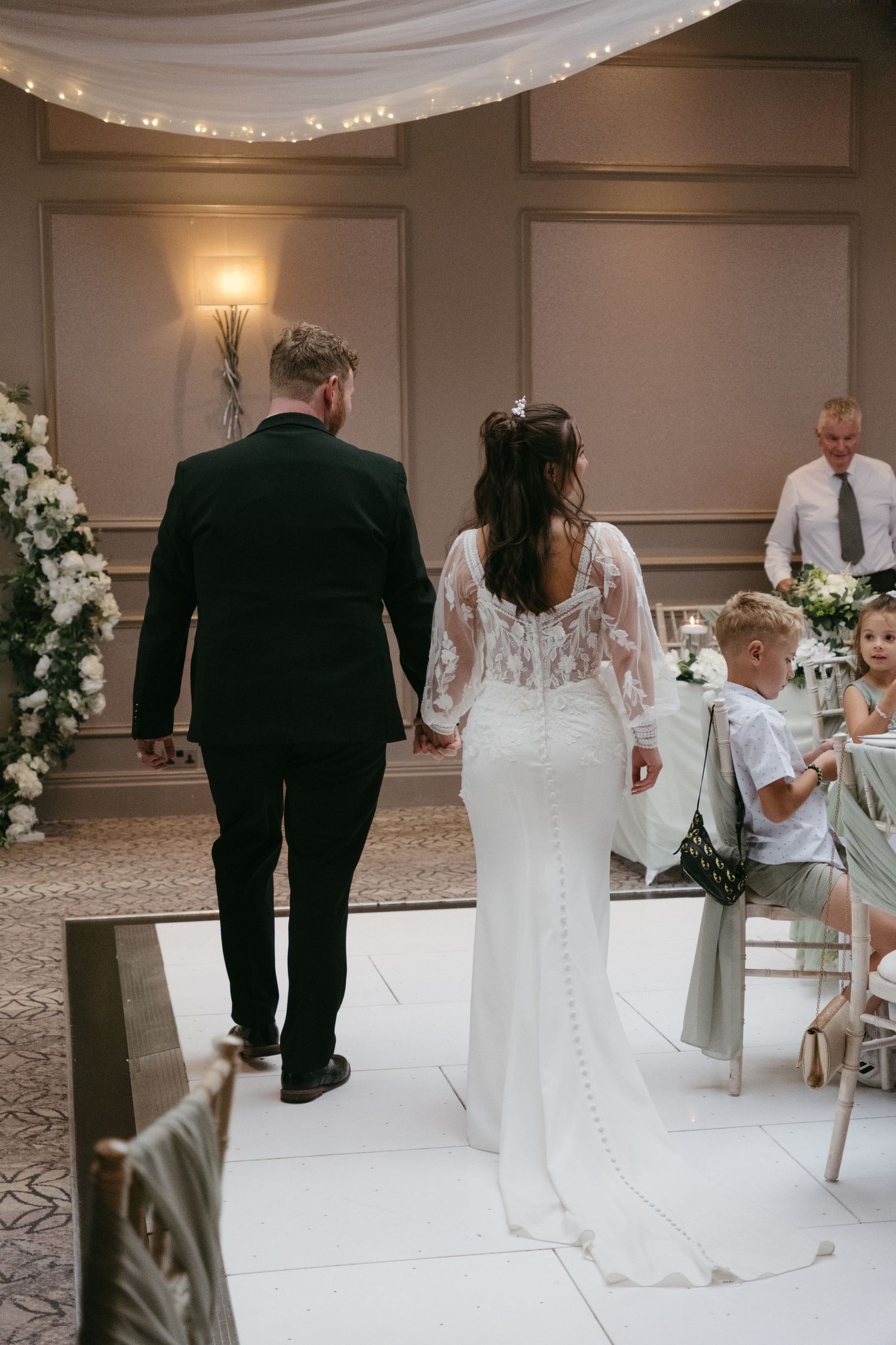 Bride and groom walking hand in hand down aisle in elegant decorated wedding reception venue.