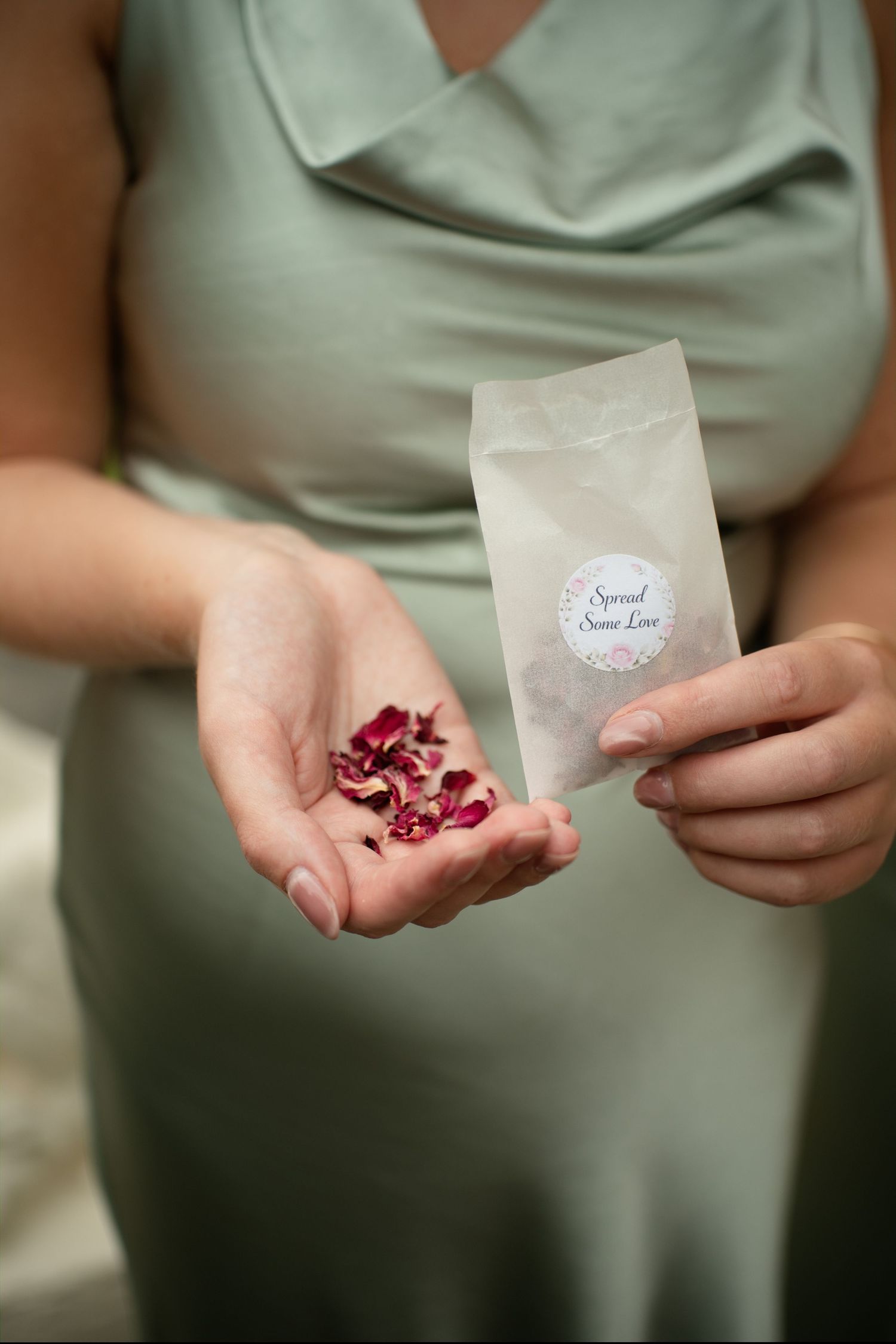 Bridesmaid in sage green dress holding confetti packet and rose petals at wedding.