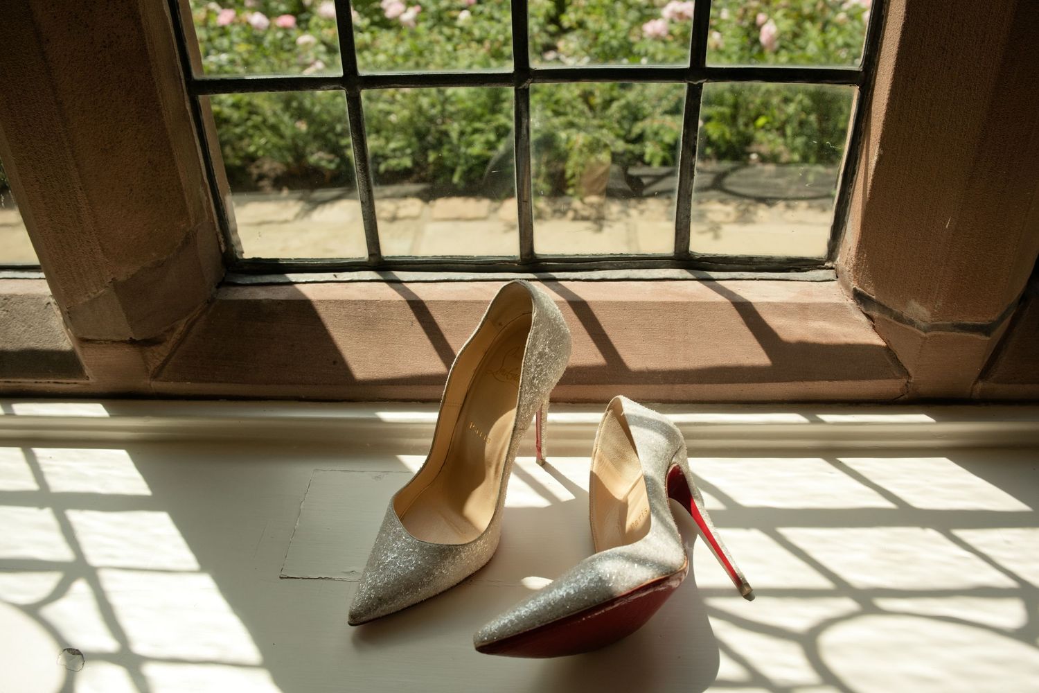 Sparkling Christian Louboutin bridal heels with red soles displayed on a windowsill in natural light.