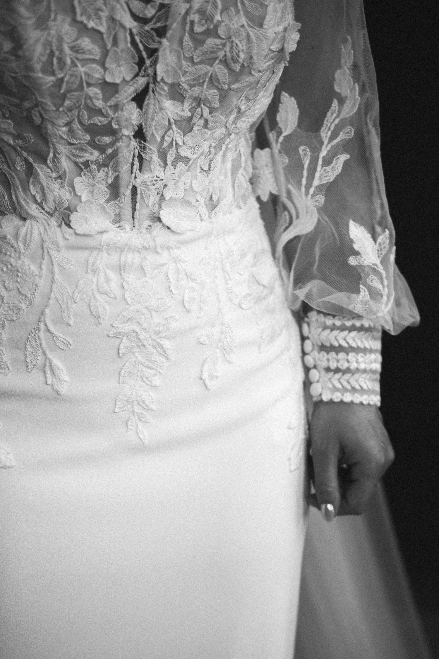 Close-up of bride in elegant lace wedding gown with pearl bracelet in black and white photo.