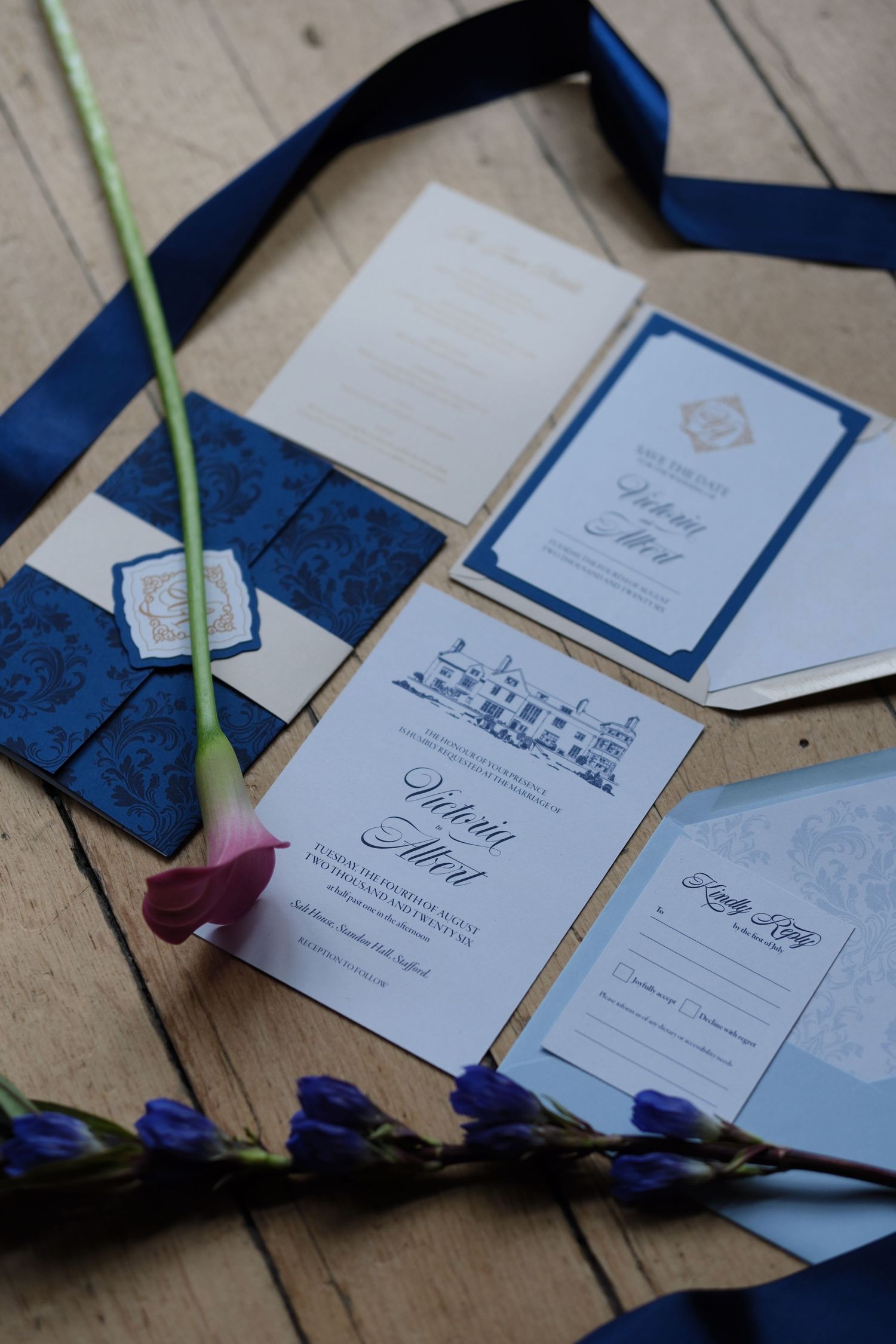 Elegant navy blue wedding invitation suite with damask envelope, menu cards, and RSVP on rustic wood with flowers.