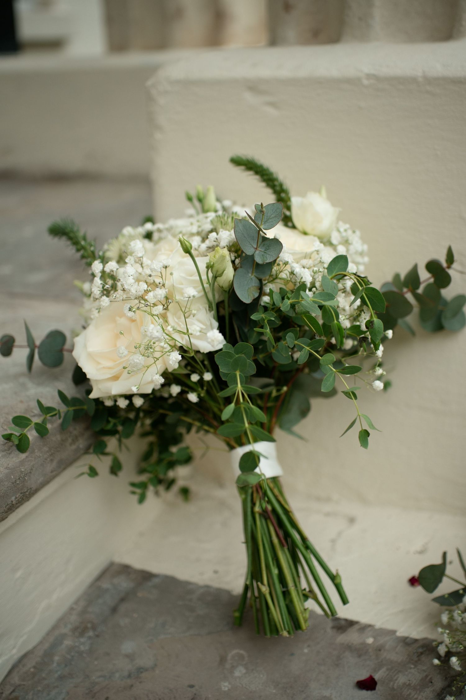 Elegant bridal bouquet of white roses, baby's breath and eucalyptus on stone steps.