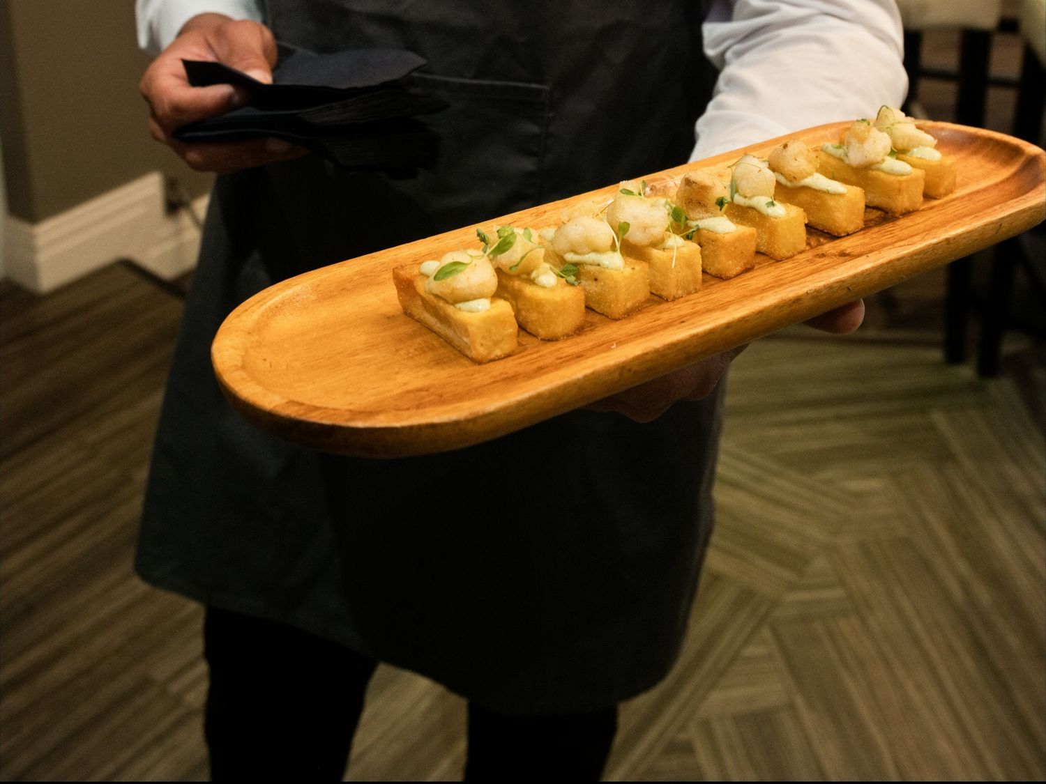 Catering server presents elegant wooden board of bite-sized appetizers at wedding reception.