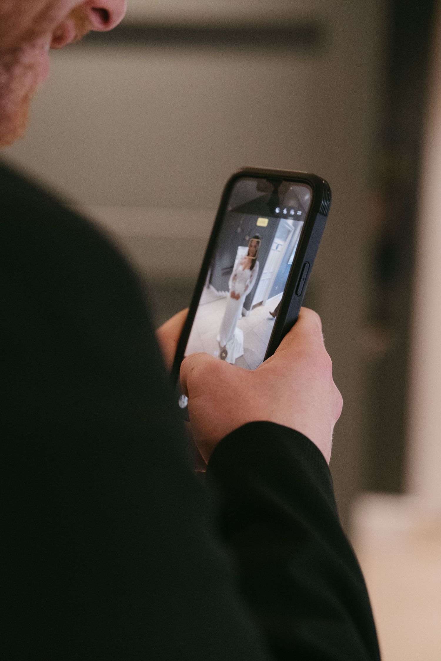 Wedding guest captures bride on smartphone camera during wedding day preparations indoors.