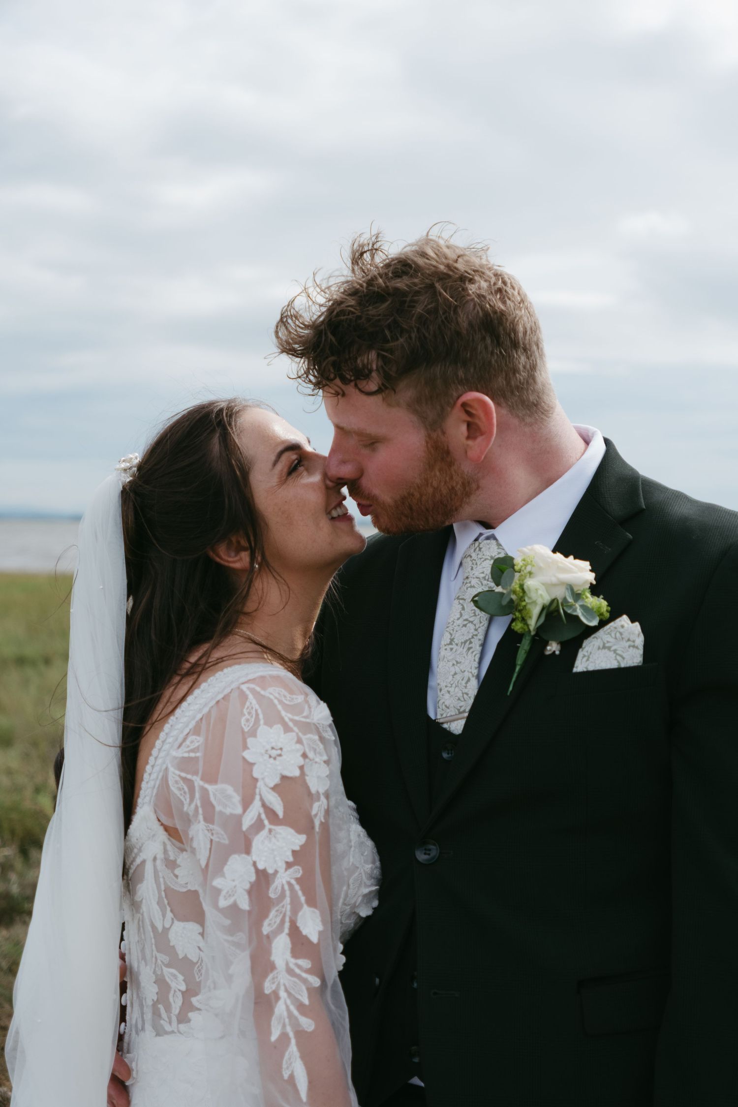 A bride and groom share a romantic moment, nearly kissing outdoors on their wedding day.