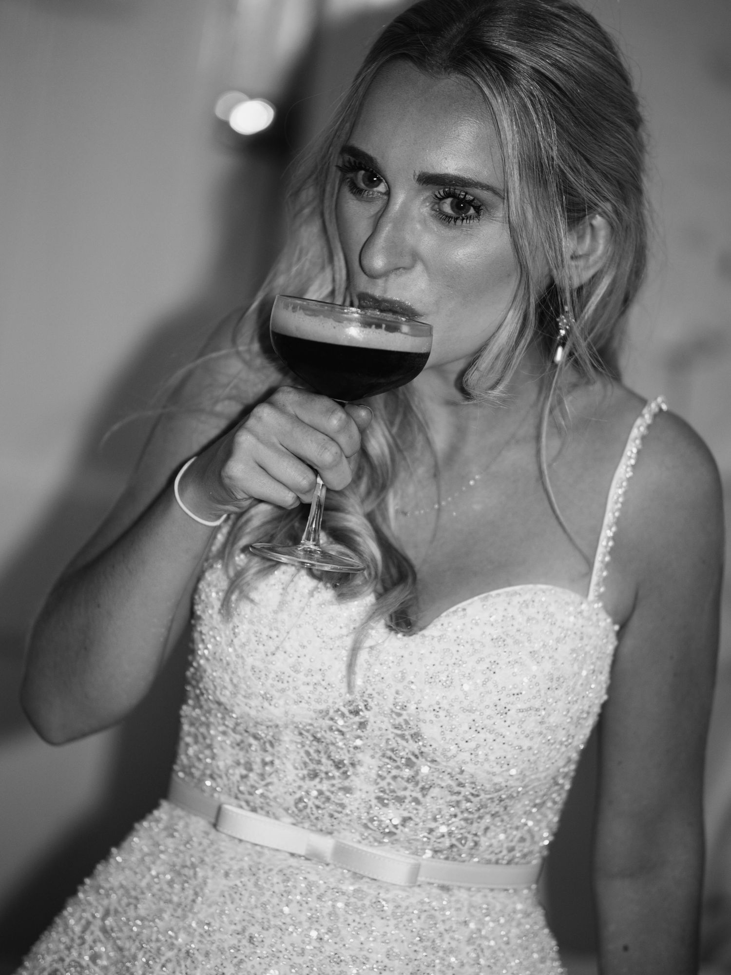 Bride in beaded gown drinks an espresso martini in a stunning black and white wedding reception portrait.
