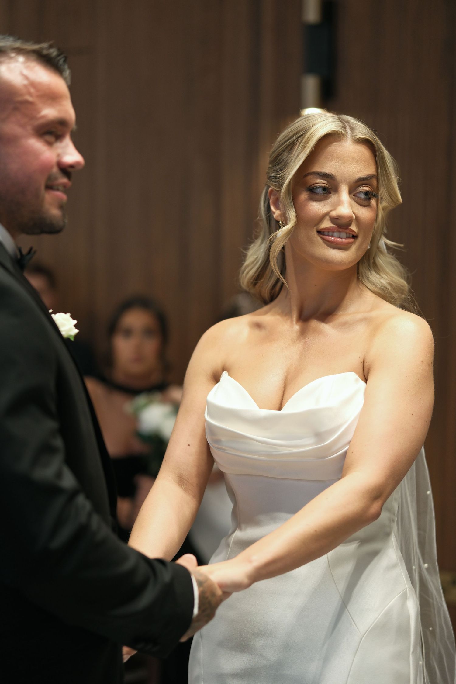 Beautiful blonde bride in strapless white gown holding hands with groom during wedding vows.