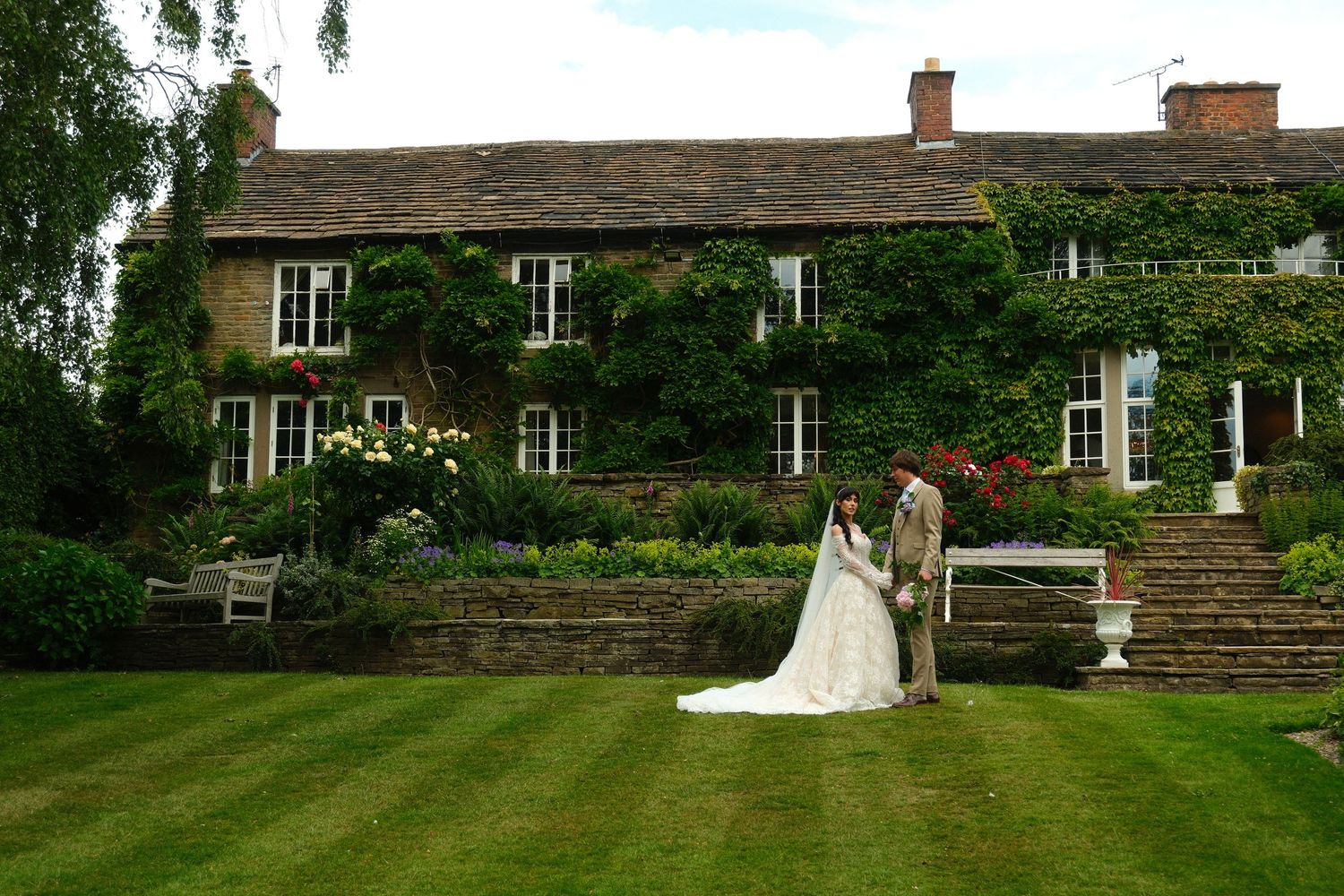 Bride and groom sharing a romantic moment on lawn before ivy-covered English country house.