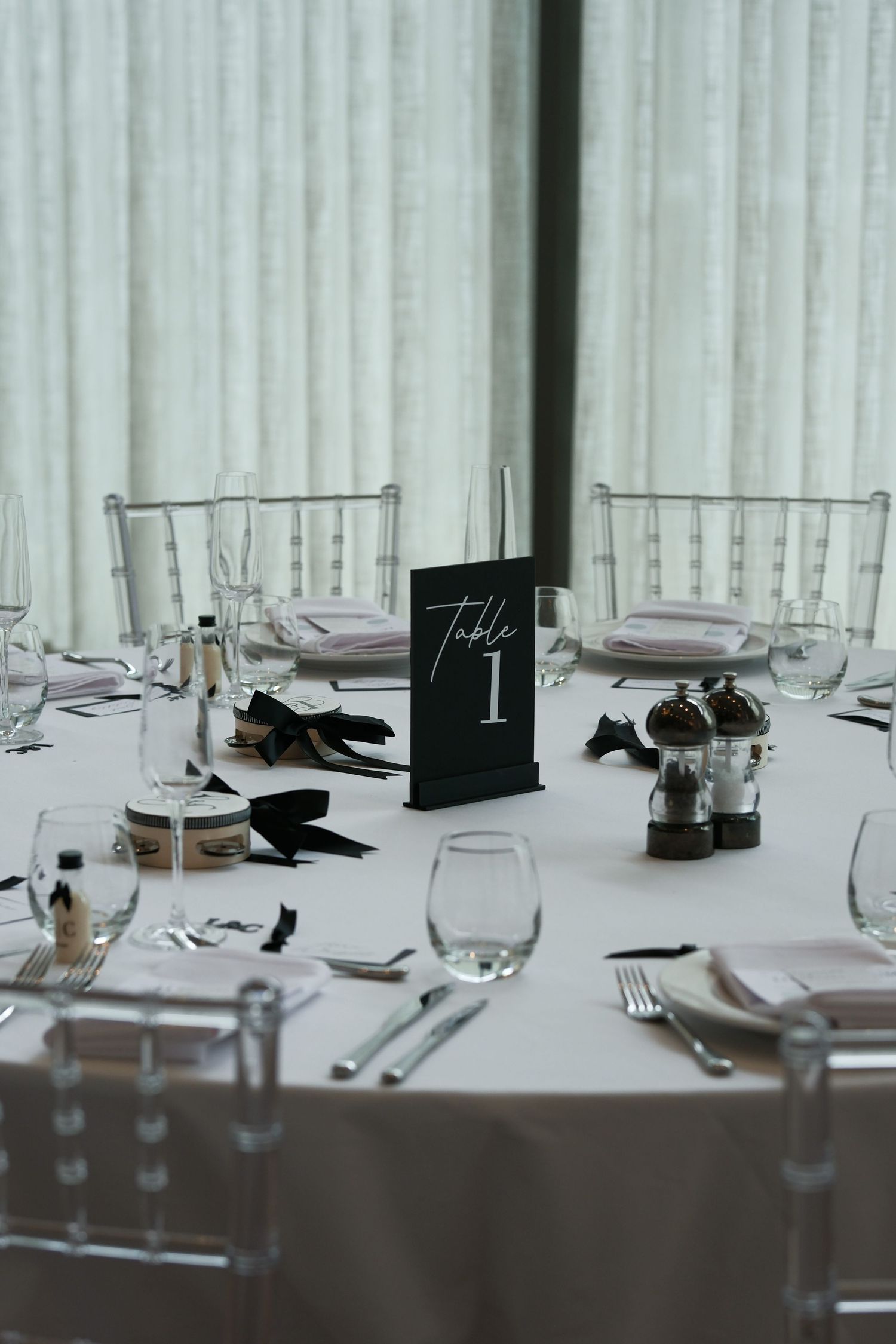 Wedding reception table elegantly set with white linens, glassware, and a black Table 1 sign.
