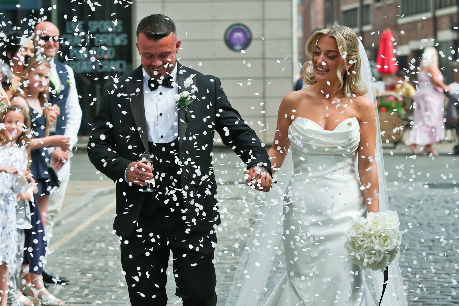 Happy newlywed couple walking through confetti shower after wedding ceremony outdoors.