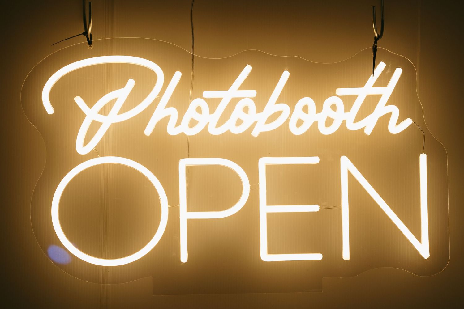 Glowing warm white neon sign reading Photobooth Open hanging against a light background.