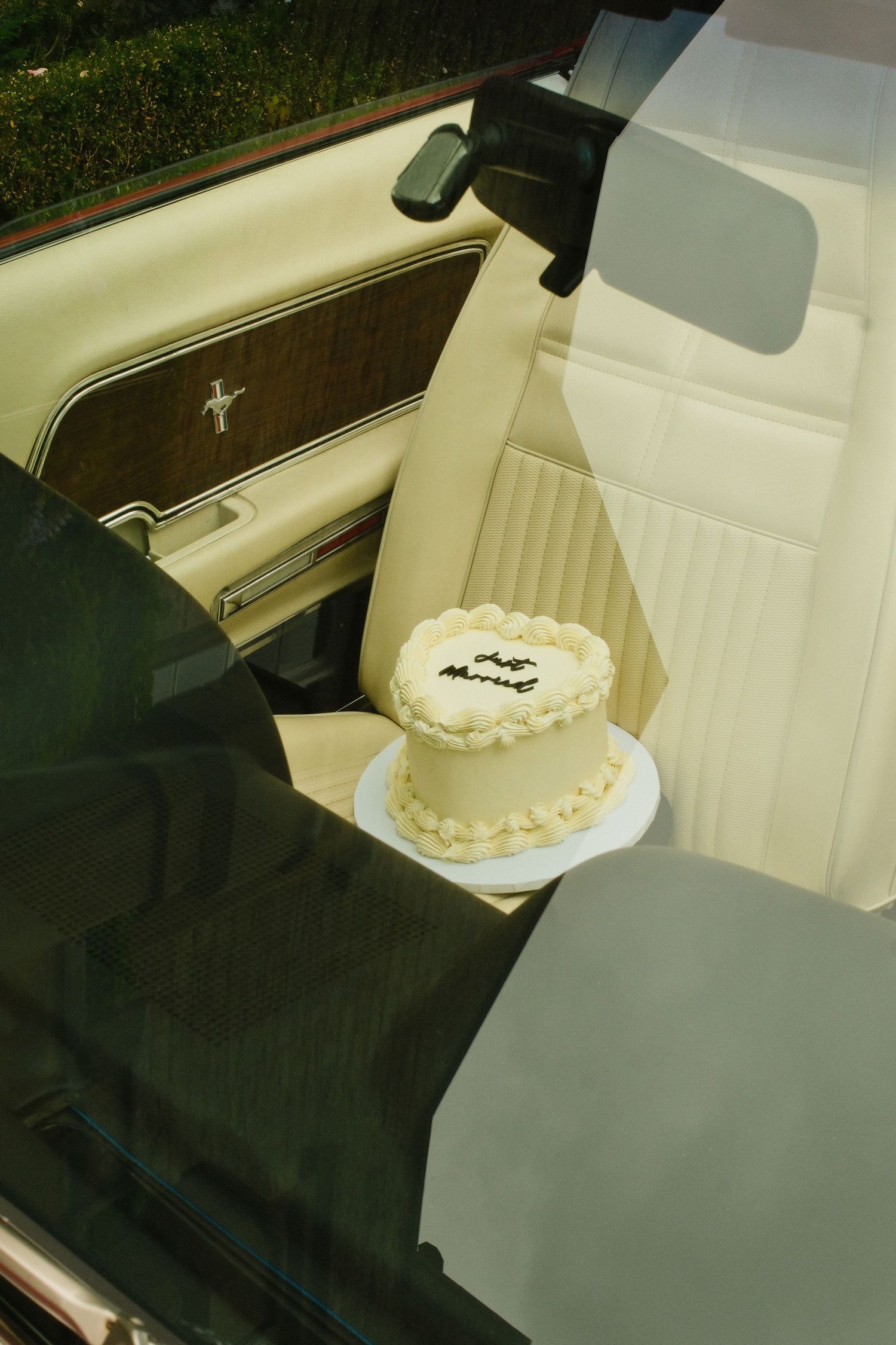 Heart-shaped wedding cake with 'Just Married' inscription sitting on the seat of a classic Ford Mustang convertible.