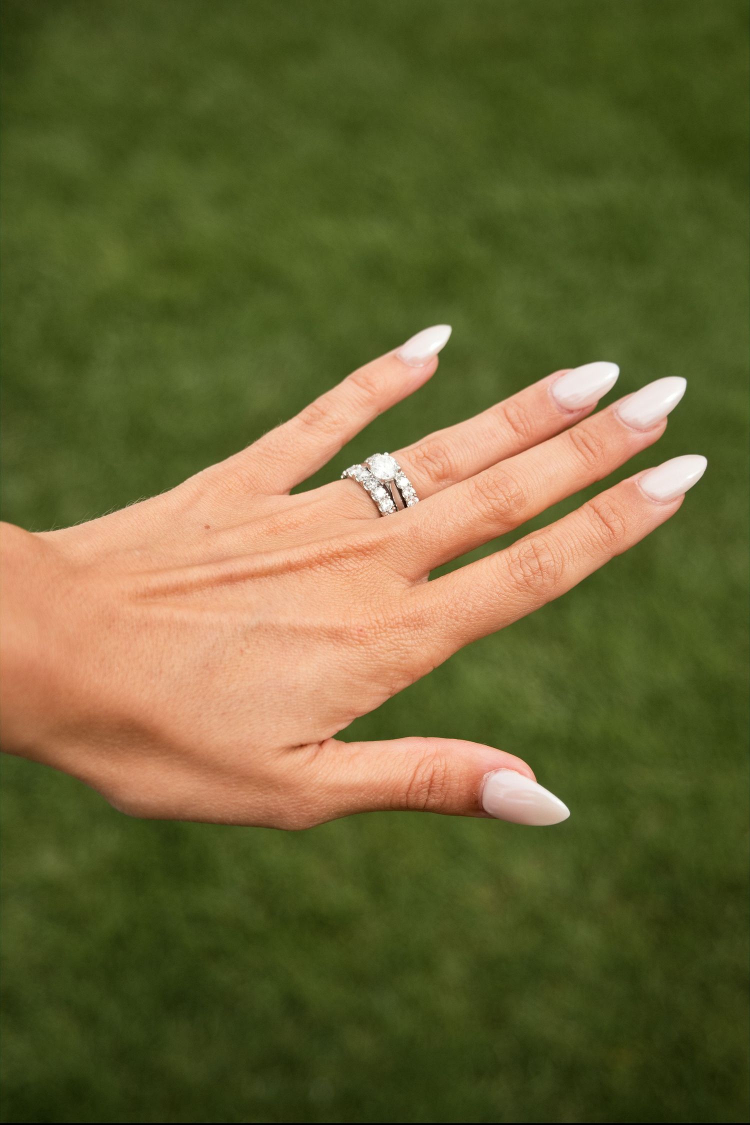 Close-up of bride's hand displaying diamond wedding rings with elegant white almond-shaped nails.