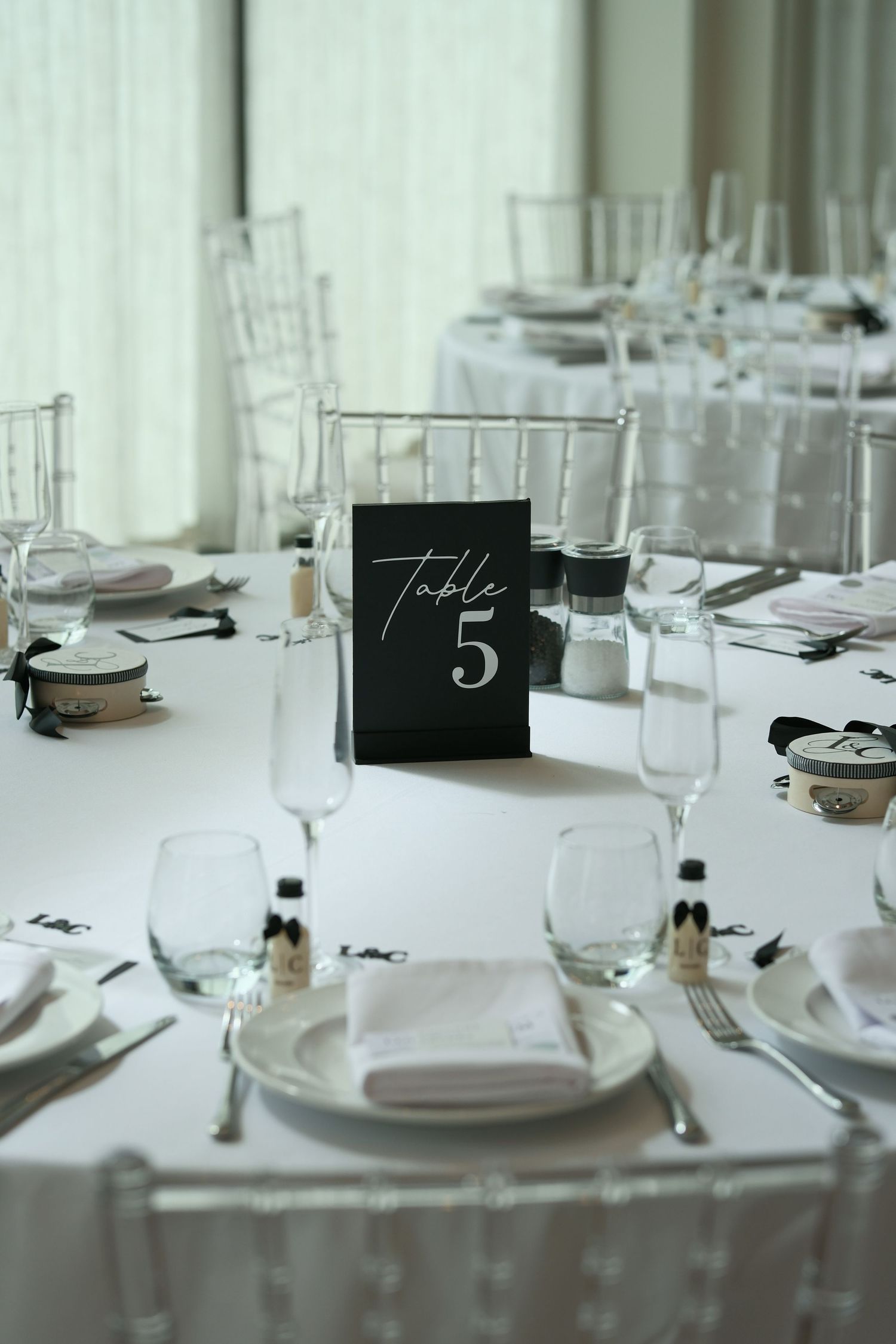 Elegant wedding reception table 5 setup with white linens, crystal glassware, silver chiavari chairs, and black table number card.