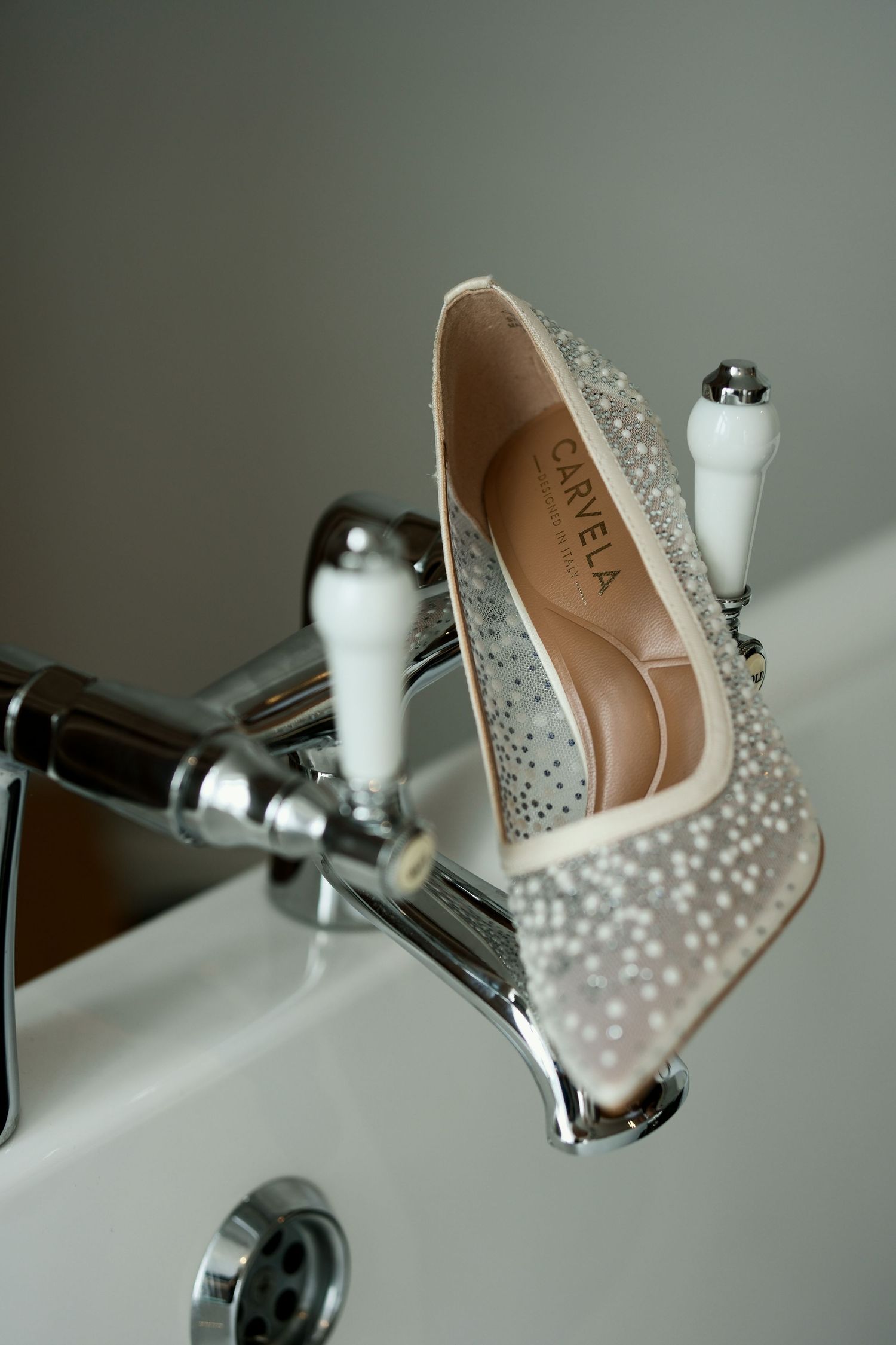 Crystal-studded Carela bridal heel balanced on vintage chrome bathroom tap faucet handles.