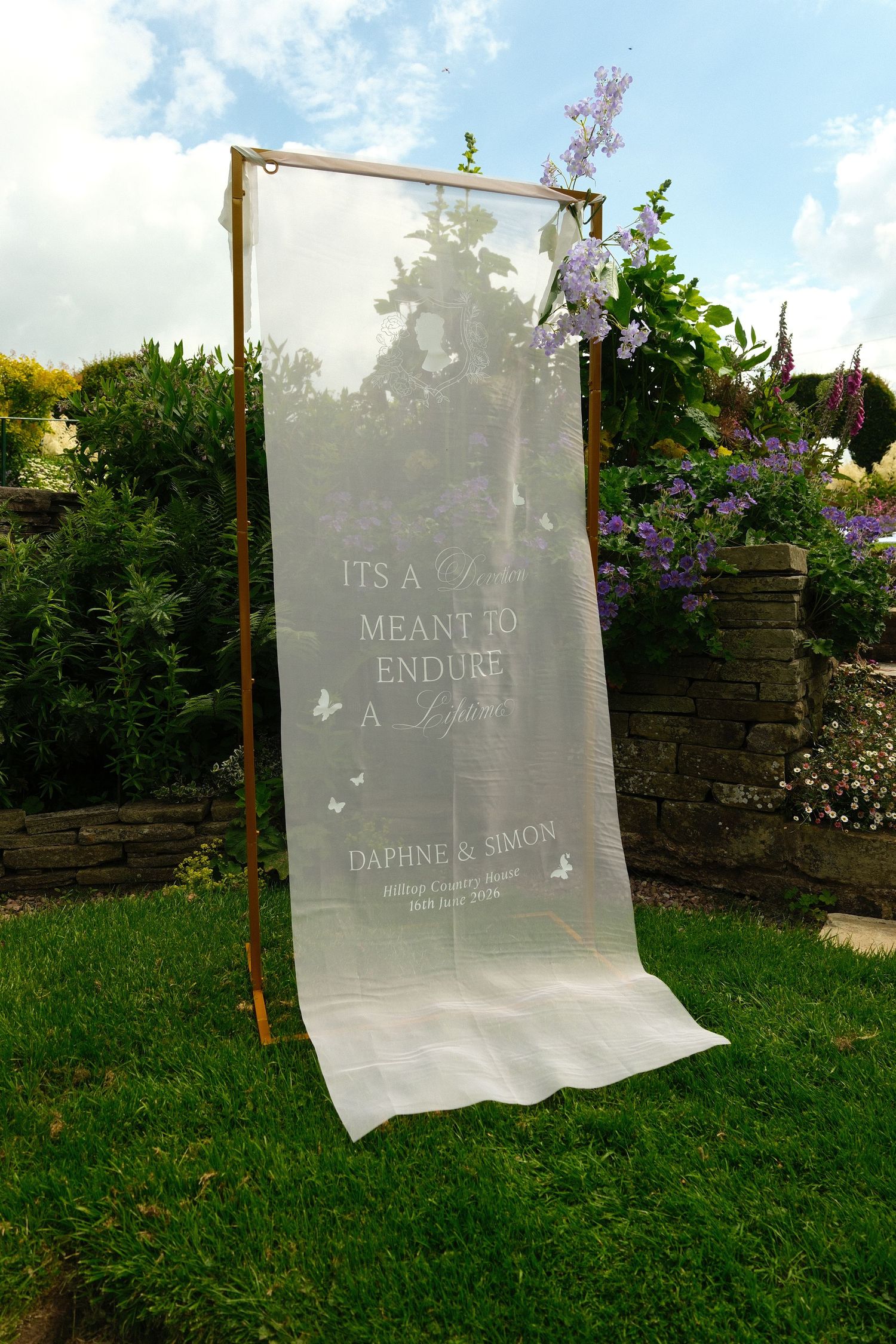 Sheer wedding banner reading Its A Meant To Endure A Lifetime for Daphne and Simon in garden.