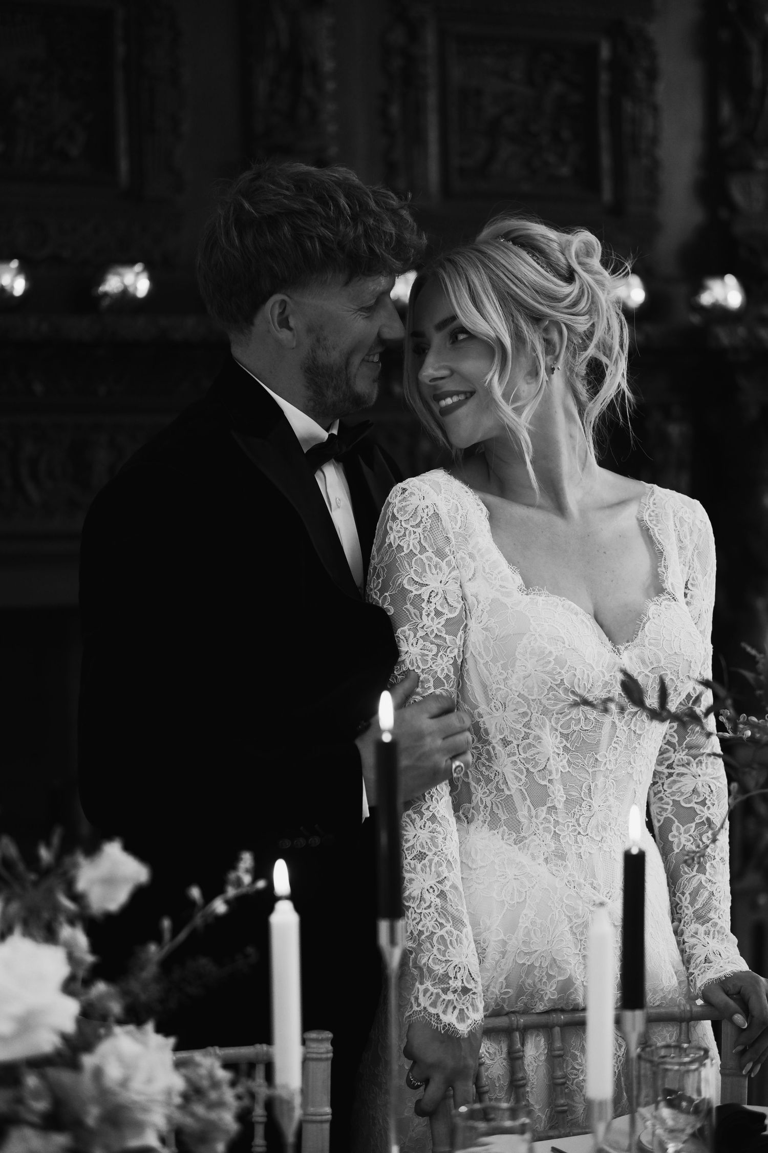 Black and white photo of a bride in lace gown and groom in tuxedo sharing an intimate moment at their wedding reception.