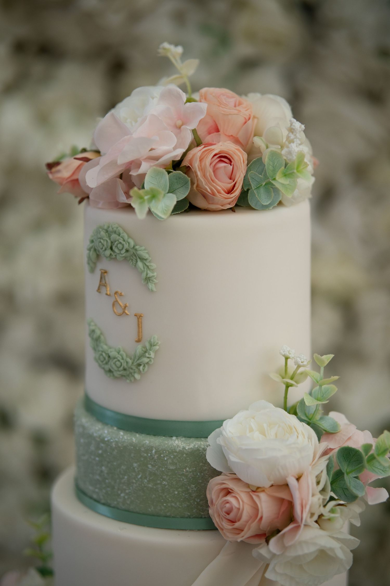 Elegant two-tier white wedding cake decorated with pink roses, succulents and monogram A&I initials.