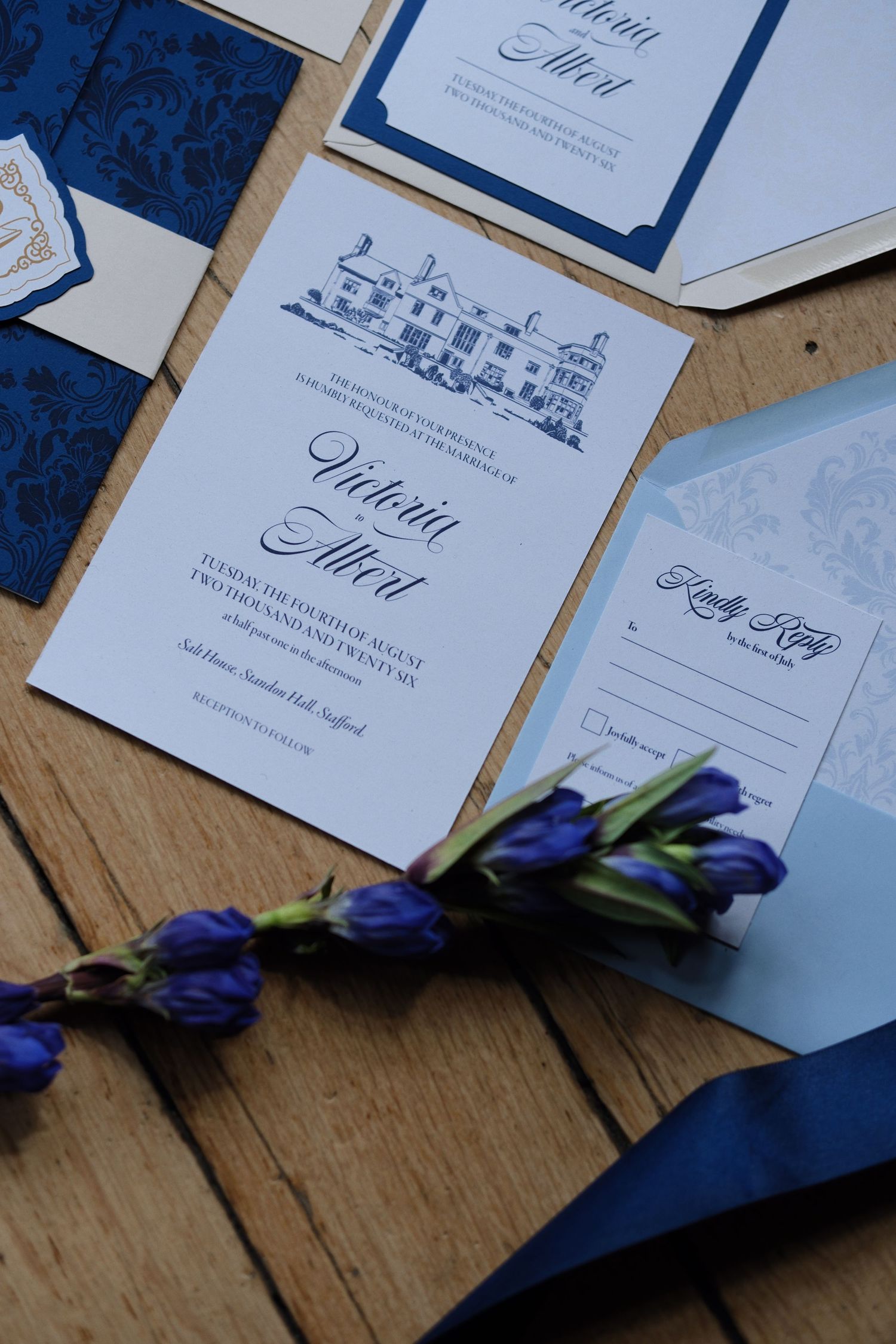 Elegant navy blue wedding invitation suite with damask details, RSVP card, and purple tulips on rustic wood.