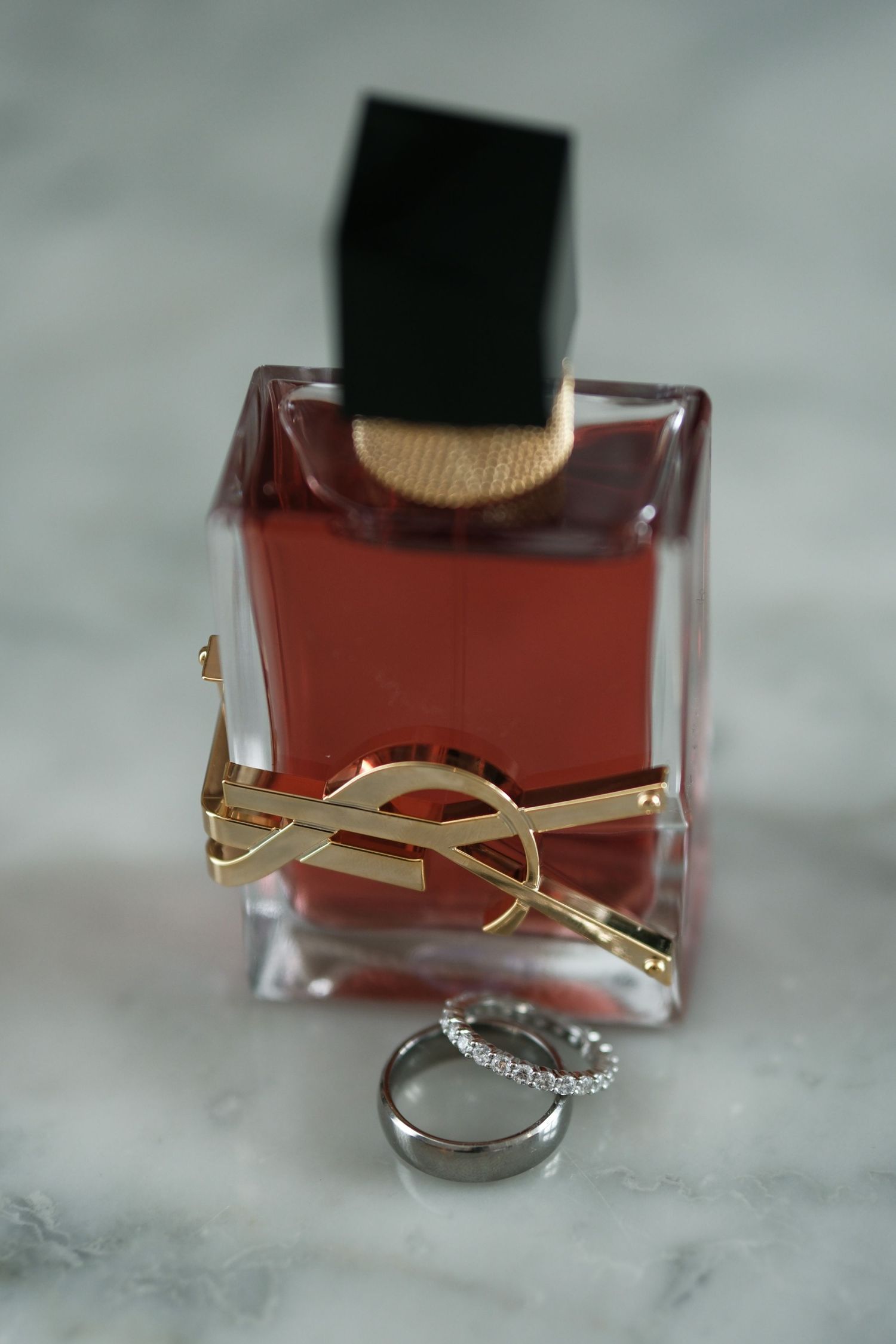 YSL Libre perfume bottle with gold logo beside elegant diamond wedding band on marble surface.