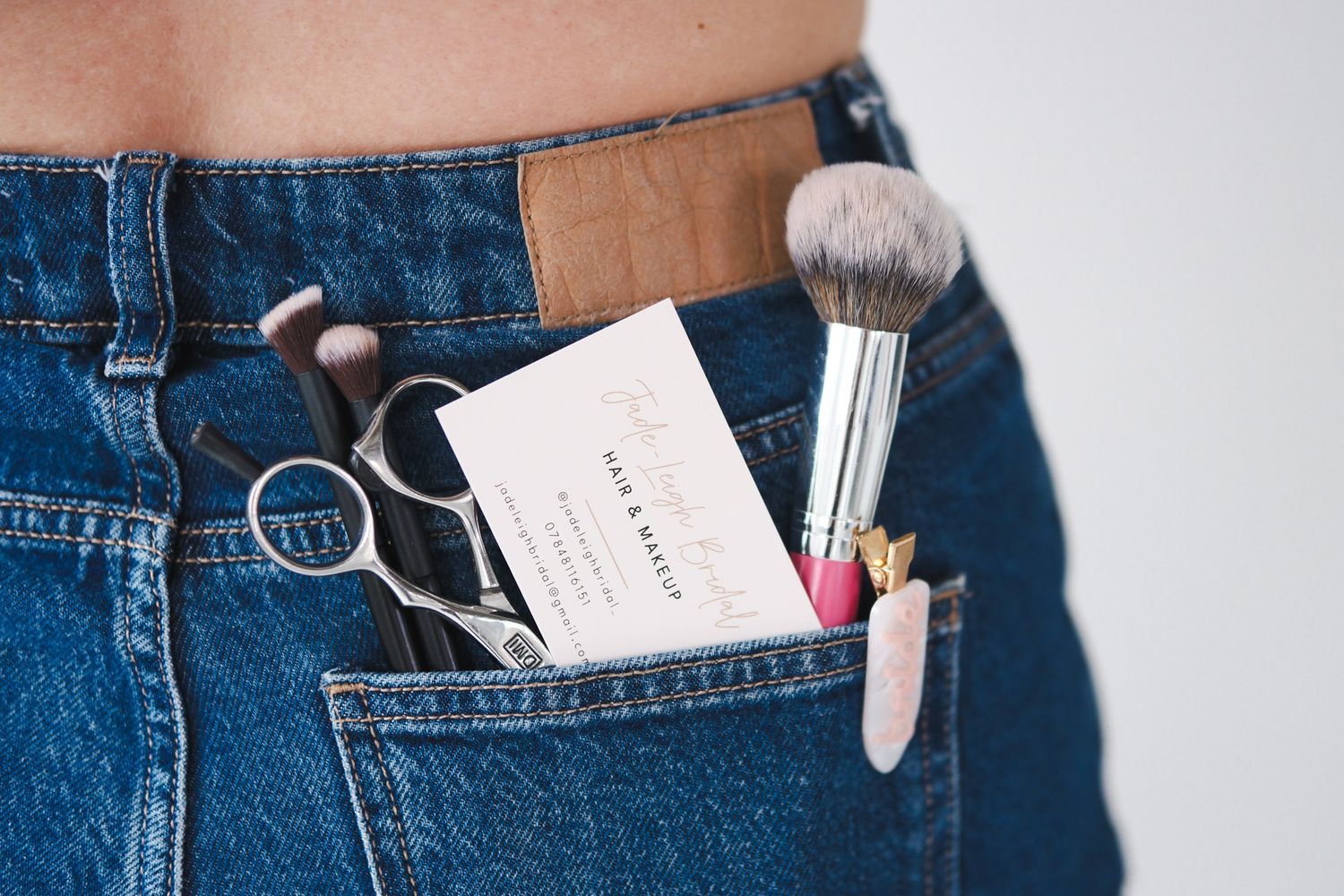 Denim jeans back pocket holding makeup brushes, scissors, and a business card.