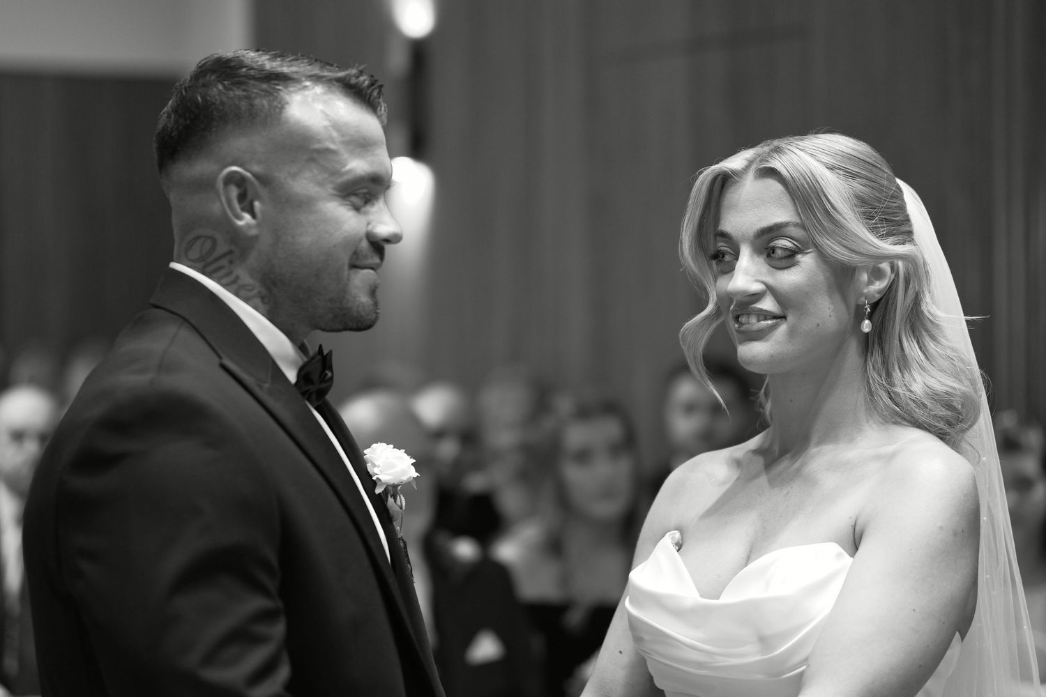 Black and white portrait of smiling bride and groom exchanging vows during wedding ceremony.