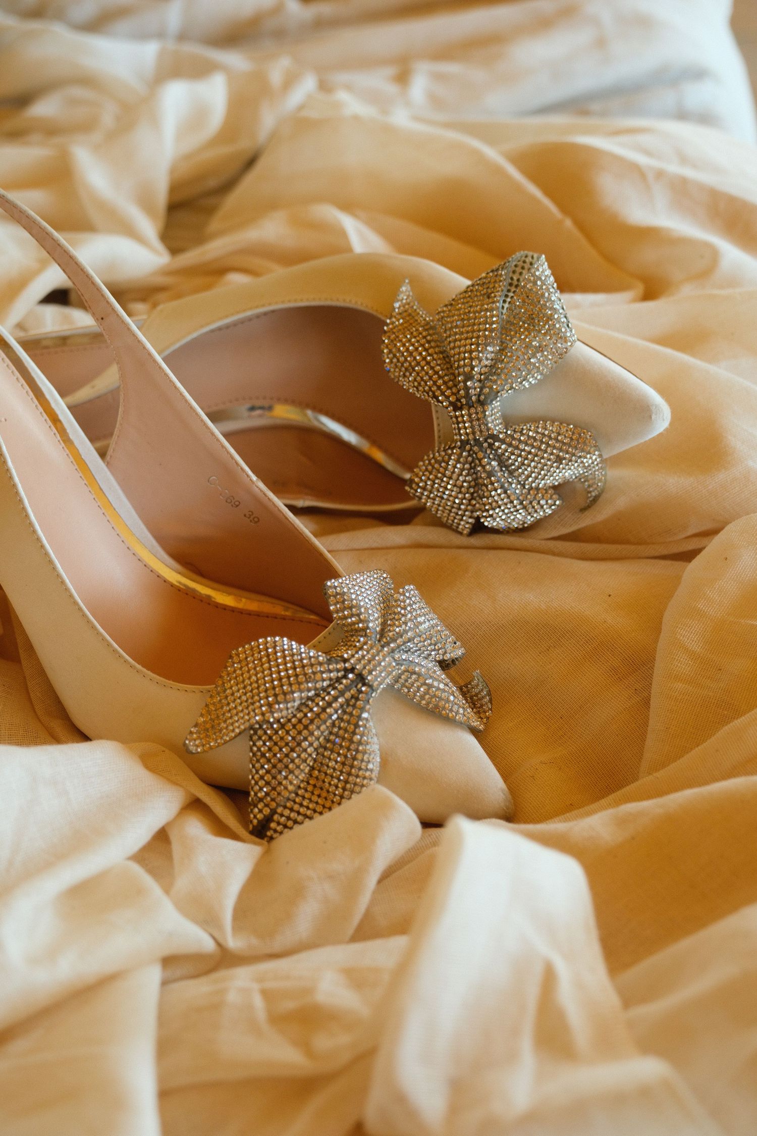 Elegant bridal heels with sparkling crystal bow embellishments resting on golden silk fabric.