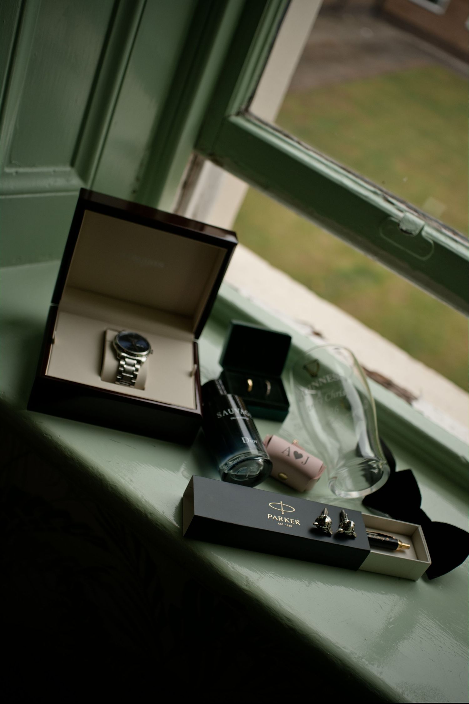 Groom's wedding accessories including watch, cufflinks, and Parker pen displayed on windowsill.