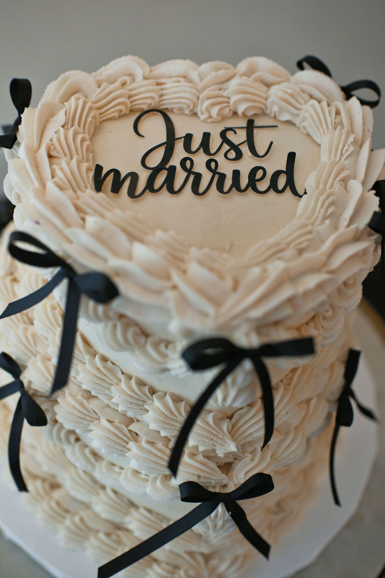 Two-tier white buttercream wedding cake with black bow decorations and a Just Married topper on heart-shaped top layer.