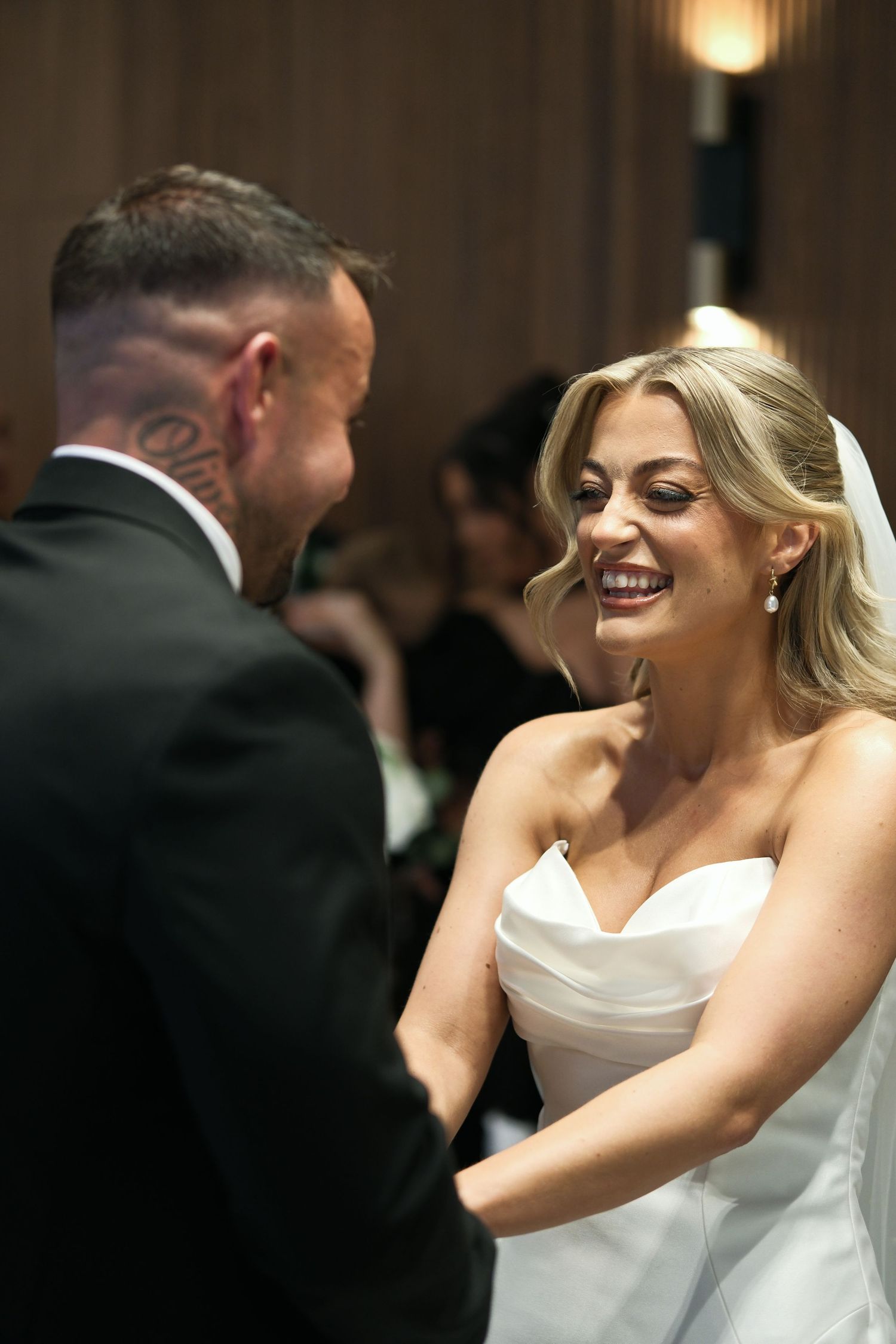 Joyful bride in strapless white gown laughing with tattooed groom after wedding ceremony.